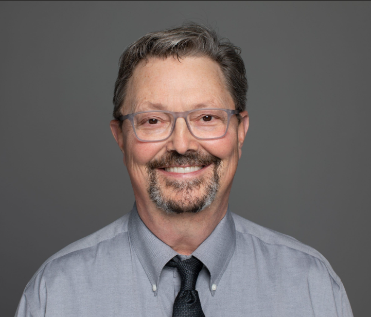 Smiling middle-aged man with glasses and a tie against a grey background