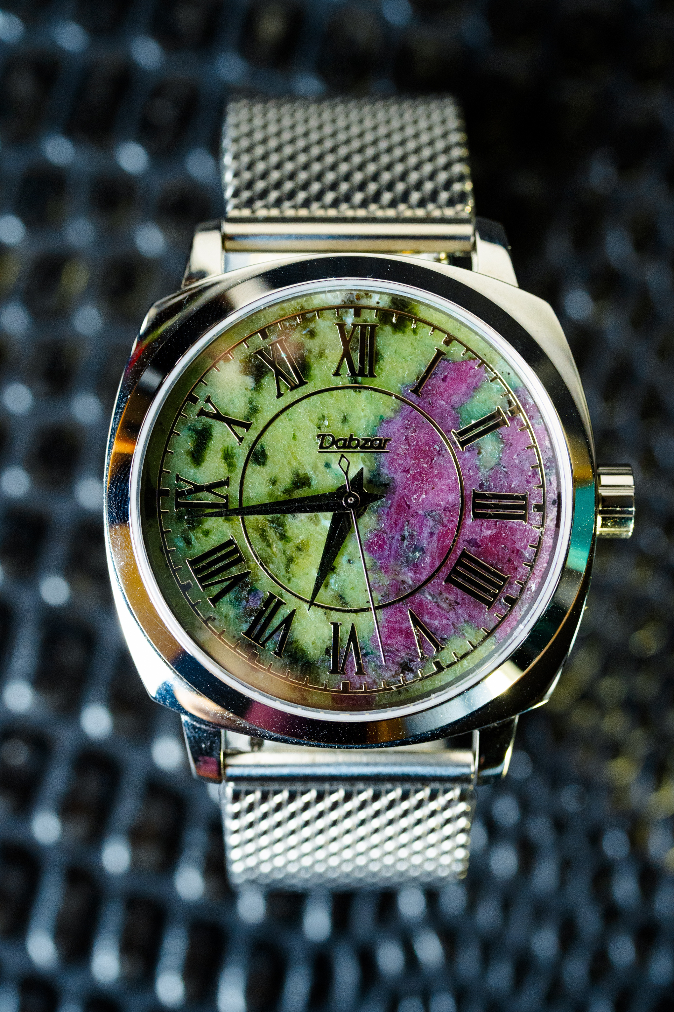 Silver watch with a colorful, marbled dial and Roman numerals on a mesh band