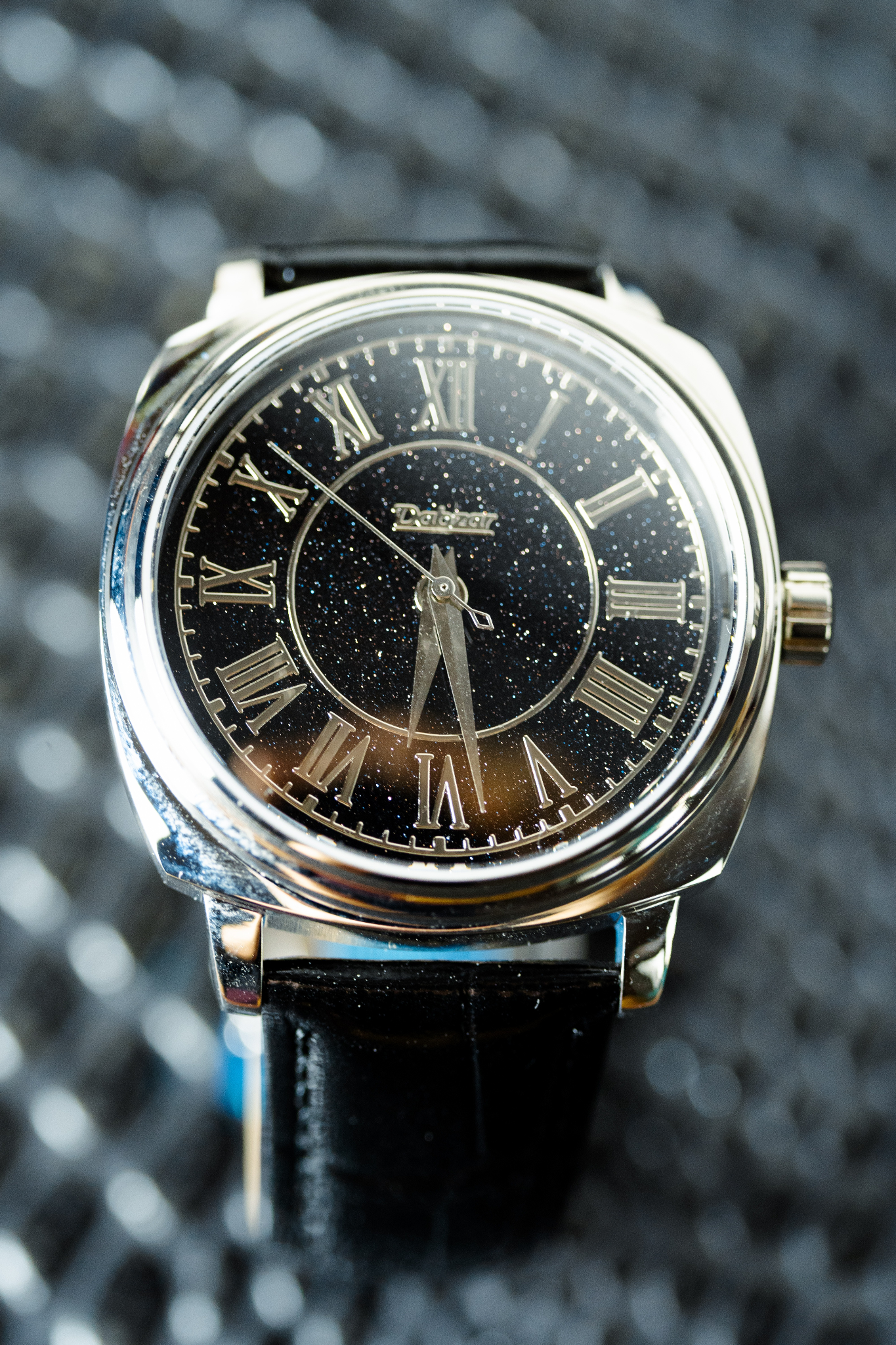 Close-up of a silver analog watch with a starry black dial and Roman numerals
