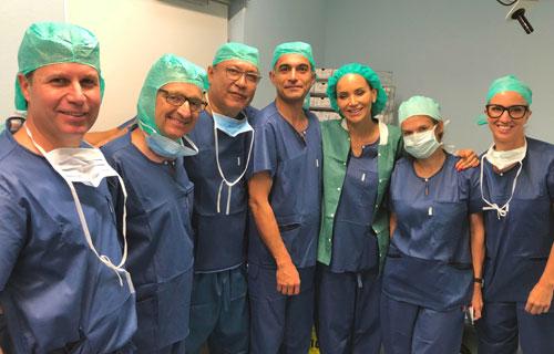 A group of seven medical professionals dressed in scrubs and surgical caps smiling together