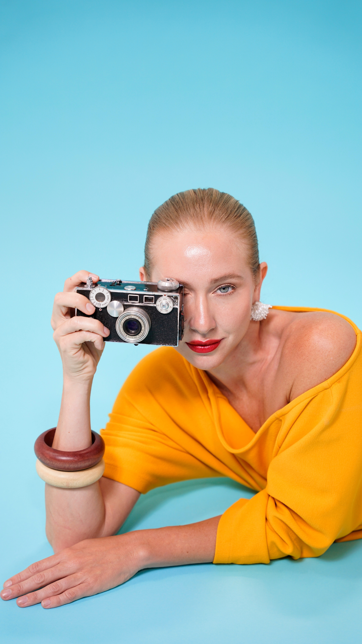 Woman in yellow top holding a vintage camera against a blue background