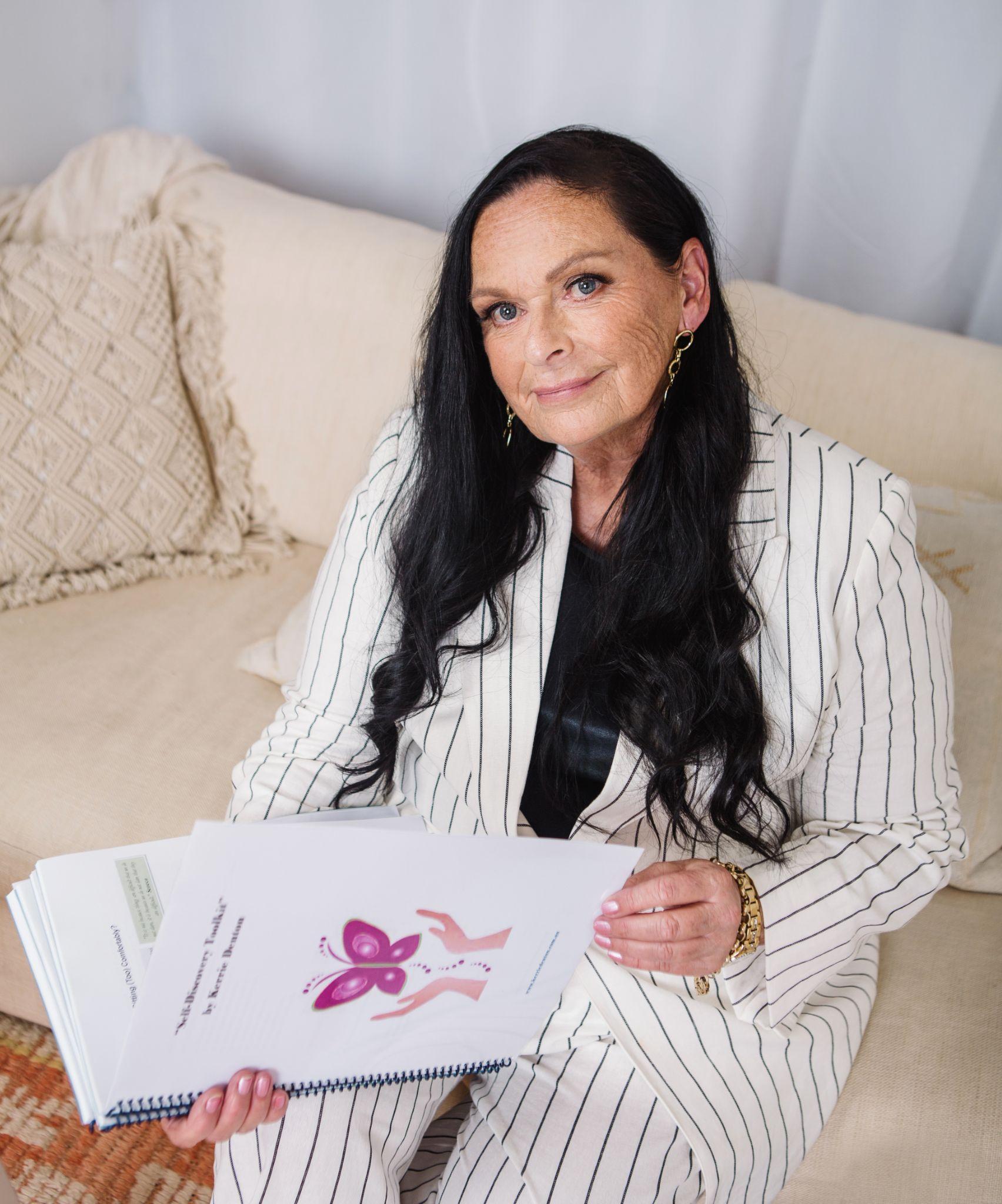 Woman in a striped suit holds a book, sitting on a beige couch