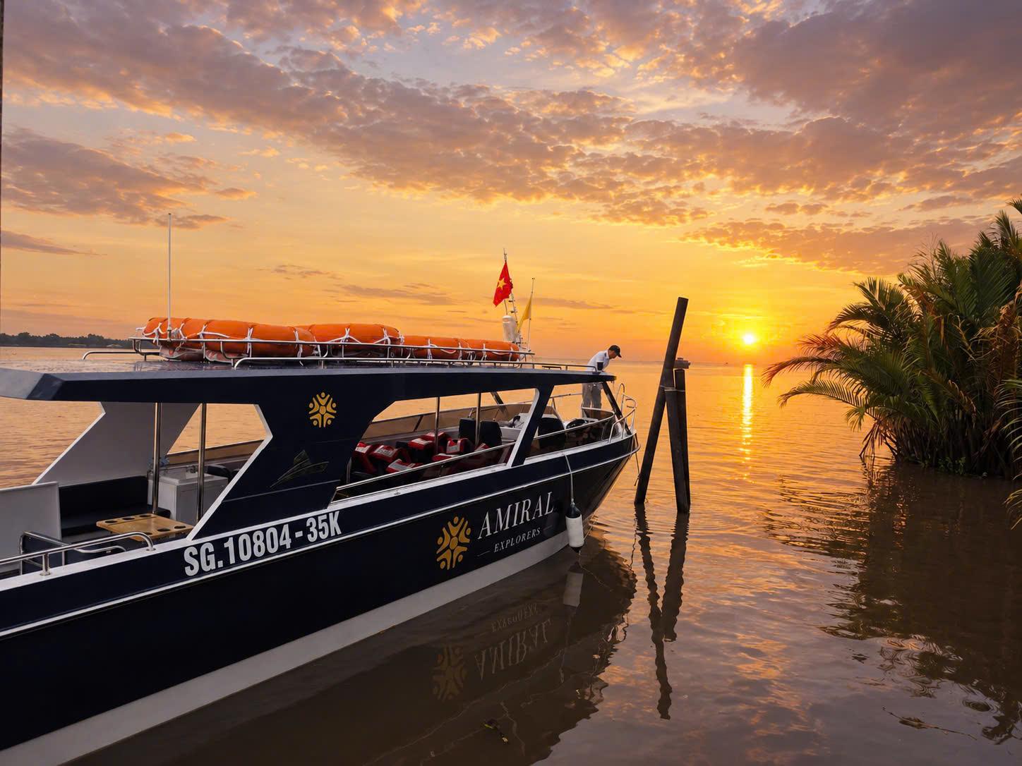 A boat docked by the shore at sunset, with colorful clouds and palm trees