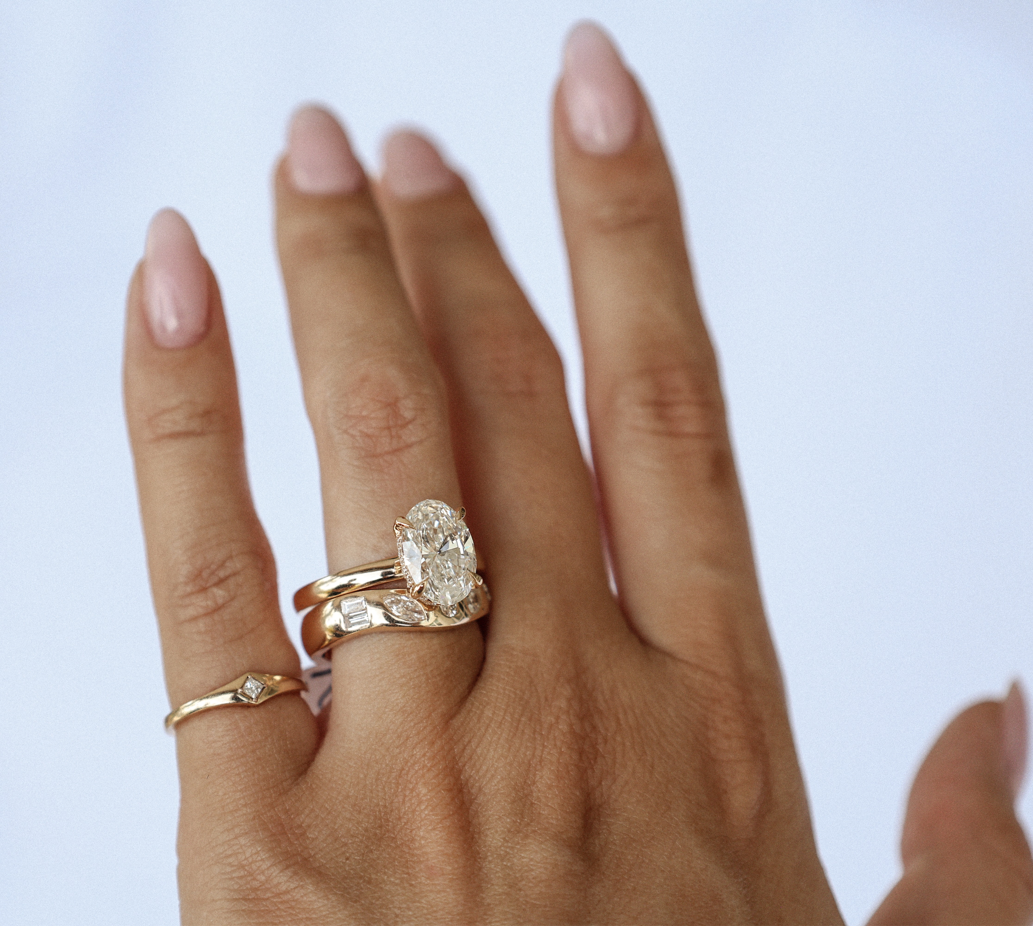 A hand with elegant rings, including a sparkling oval diamond centerpiece.