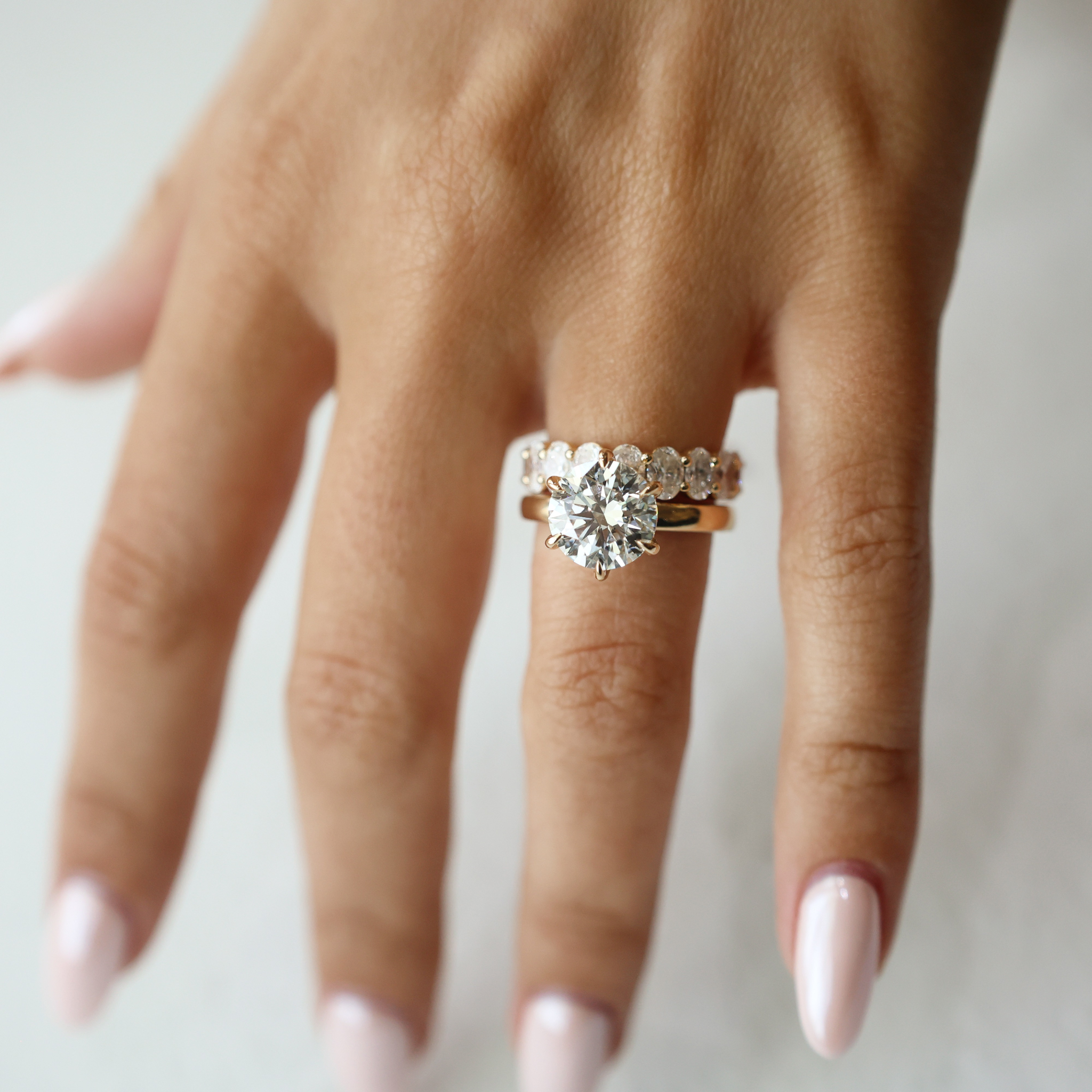 A hand with a sparkling engagement ring and a matching band, nails manicured light pink