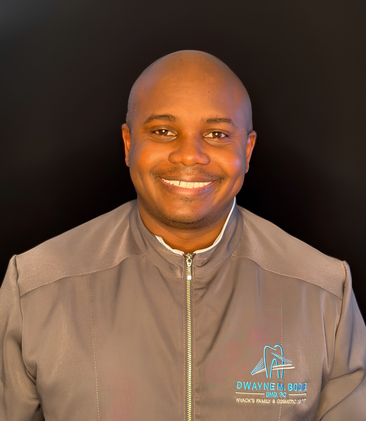 Smiling man in a gray medical jacket with embroidered name and logo