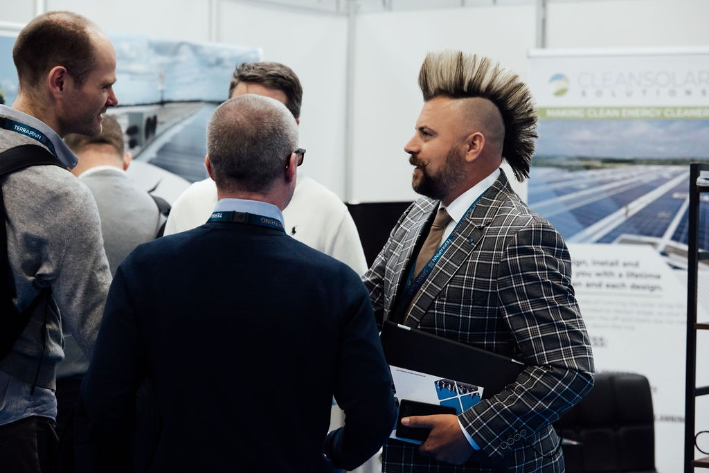 A group of professionals conversing at a clean energy expo, one with a mohawk hairstyle