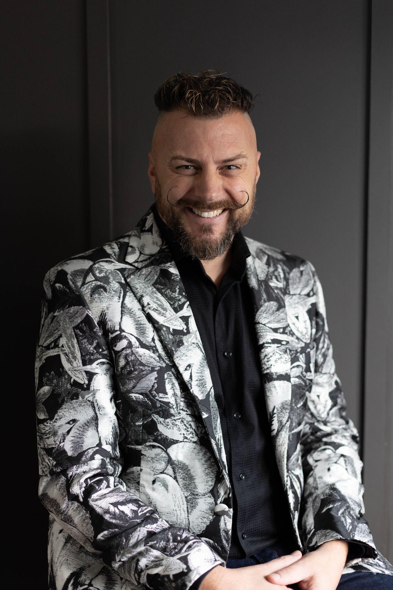 Man with a stylish patterned suit smiles warmly while posing against a gray background
