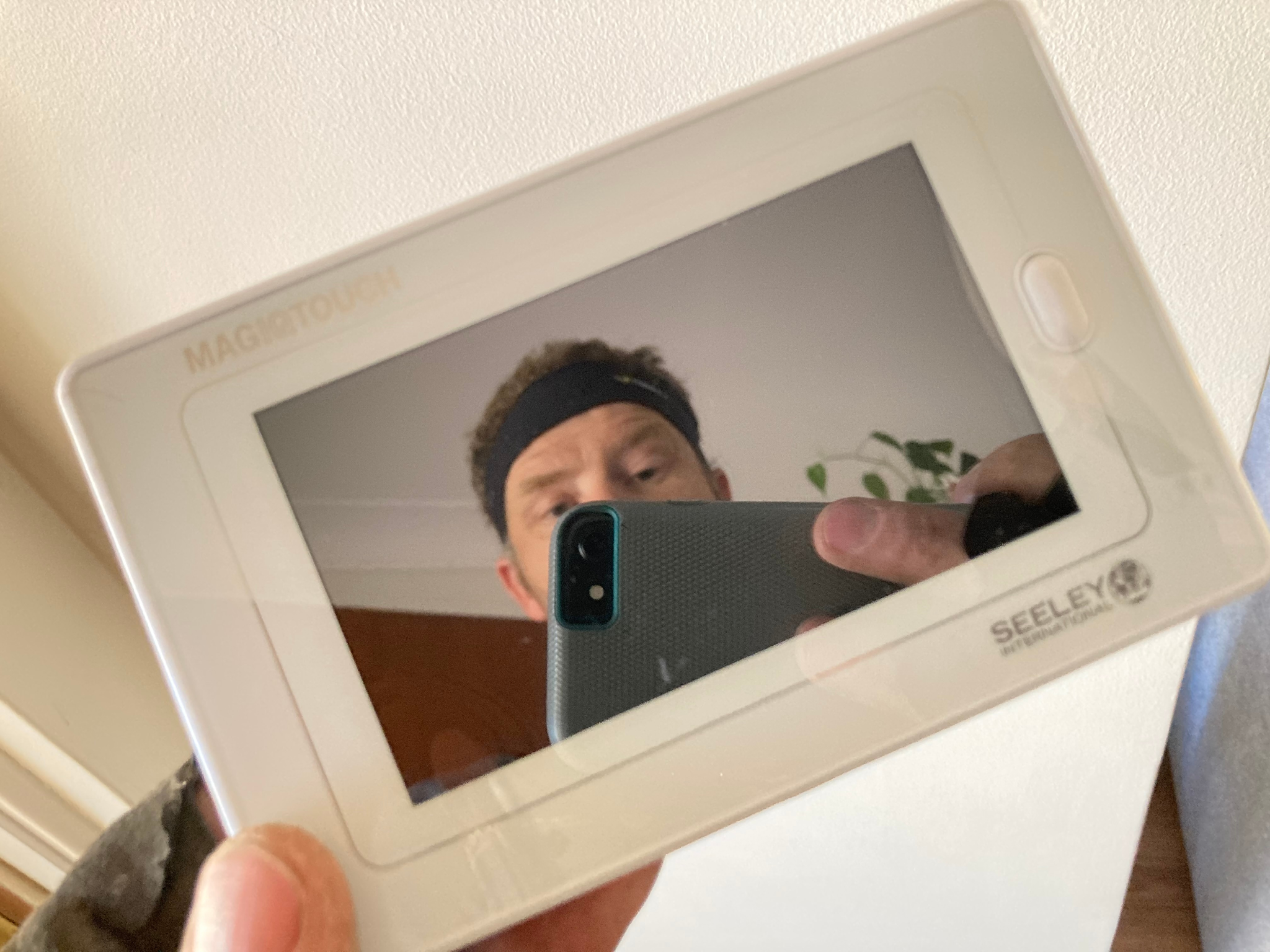 A person holding a white device with a reflective screen, capturing their image.
