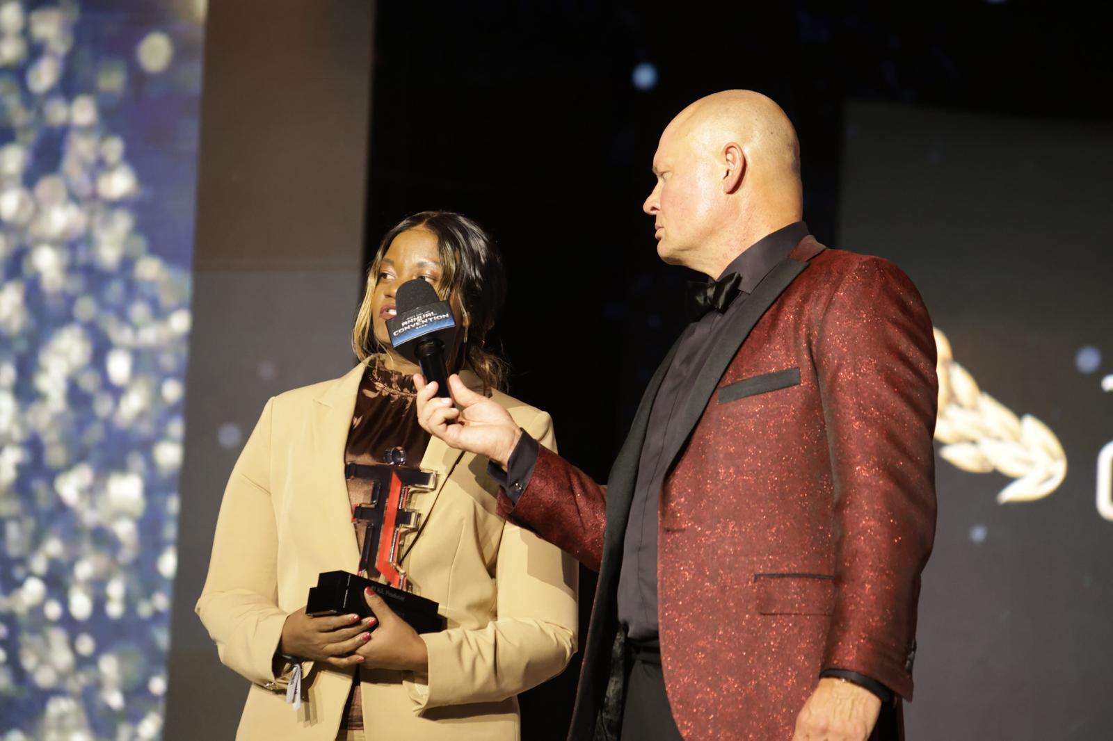 A woman receives an award while a man interviews her on stage
