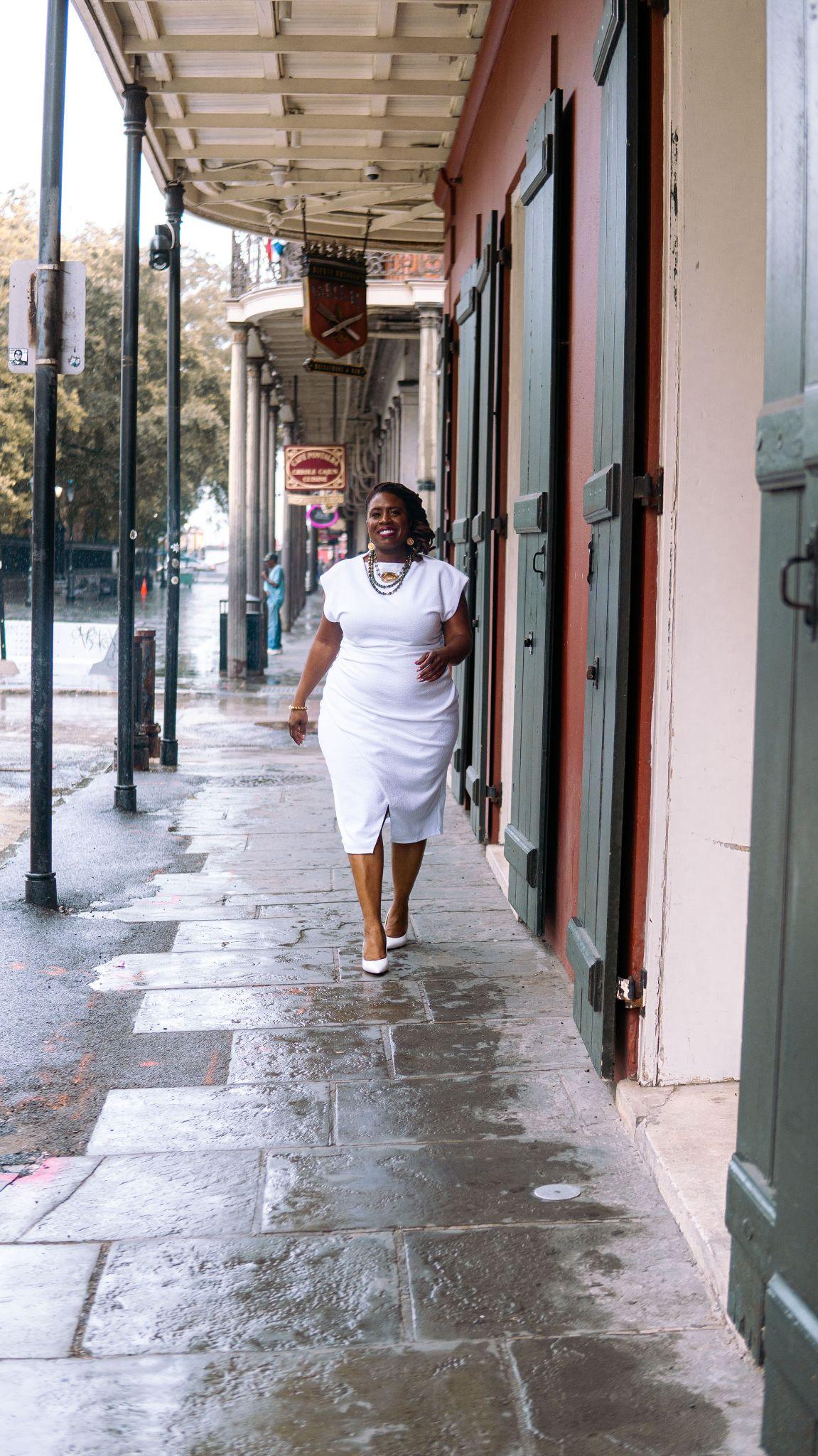 Woman in a white dress walking on a rain-soaked street with shutters