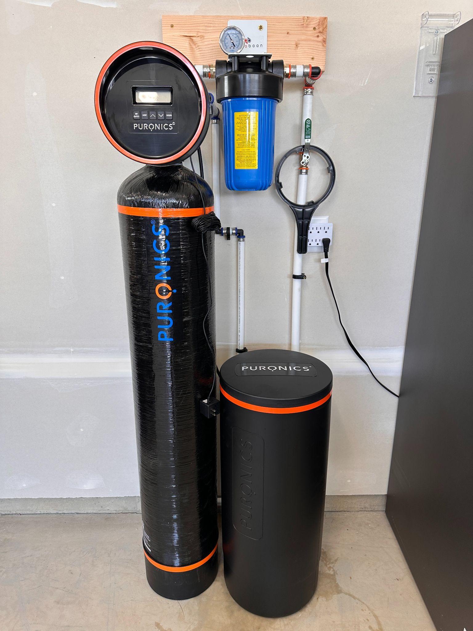 Water filtration system with a black tank, control display, and blue filtration unit mounted on wall