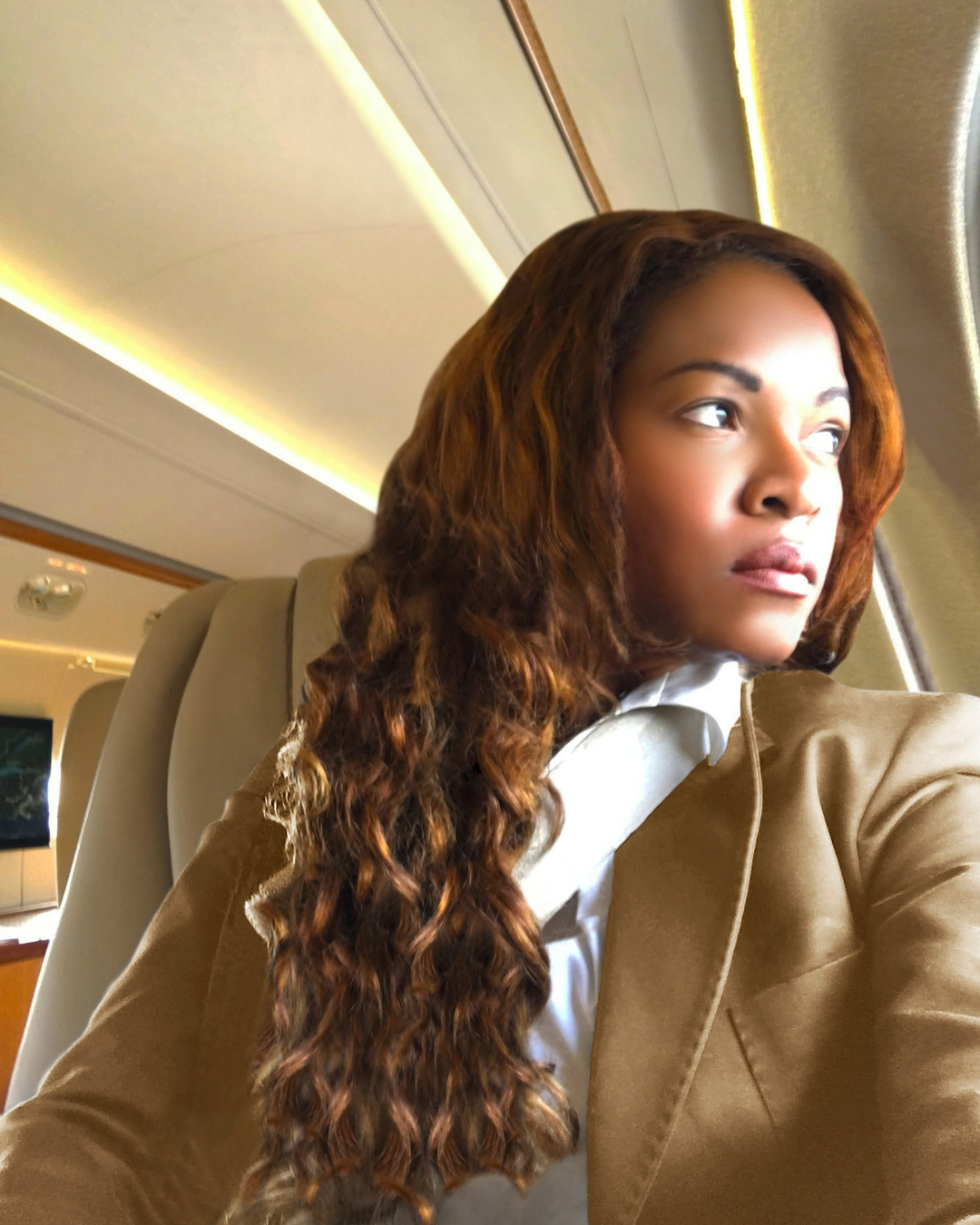 A person with long, wavy hair poses in a private jet interior.