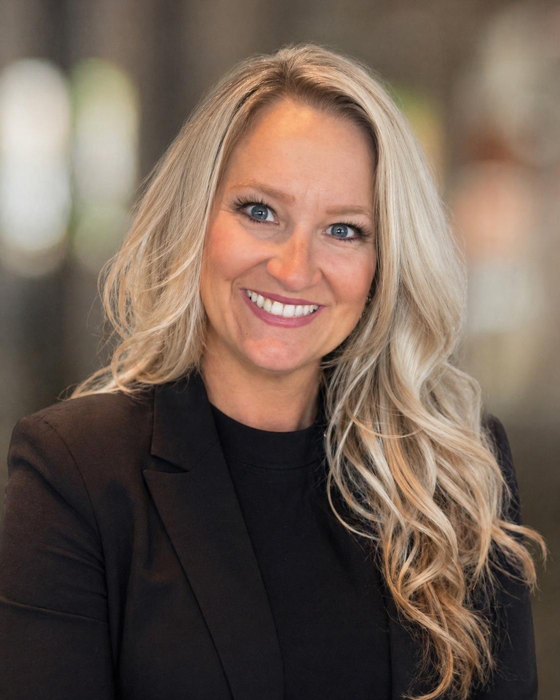 Smiling woman with blonde hair wearing a black blazer in a professional setting