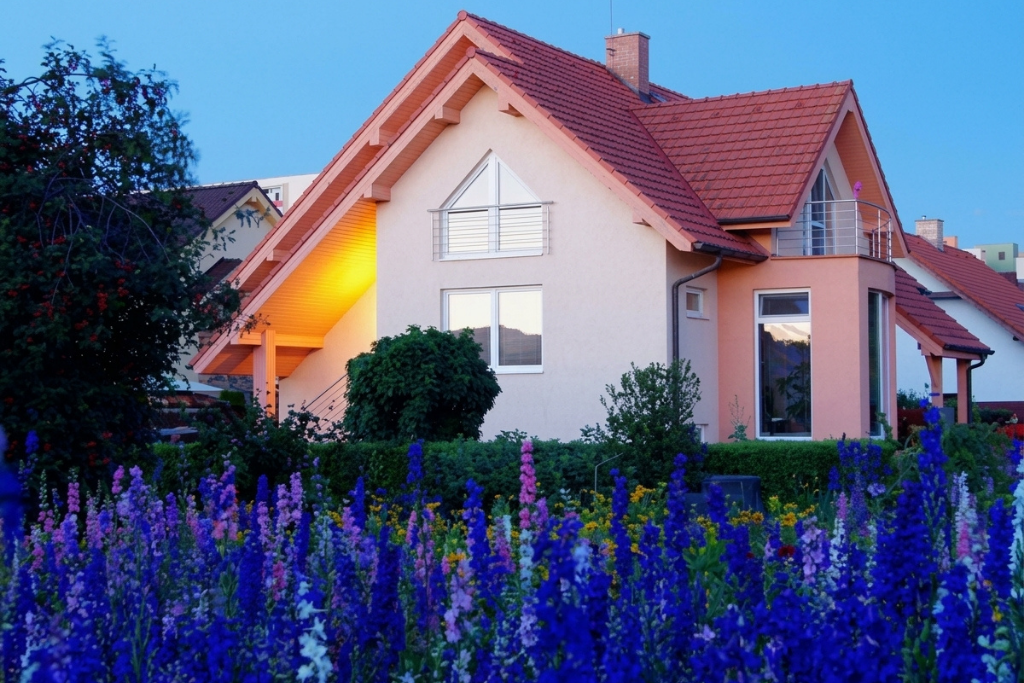 A cozy house with a red roof surrounded by colorful flowers at dusk