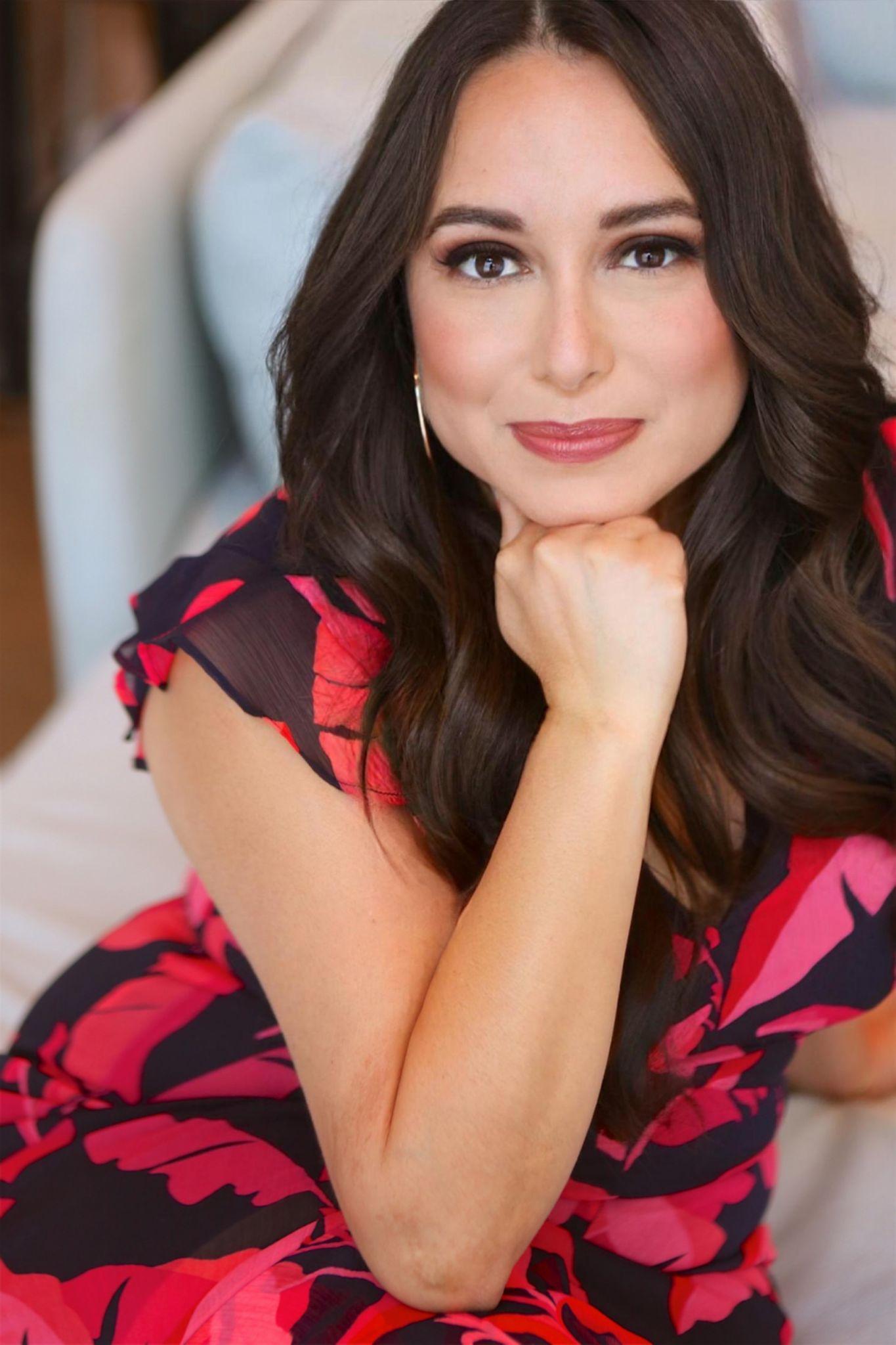 Woman in a floral dress sitting on a couch, resting her chin on her hand