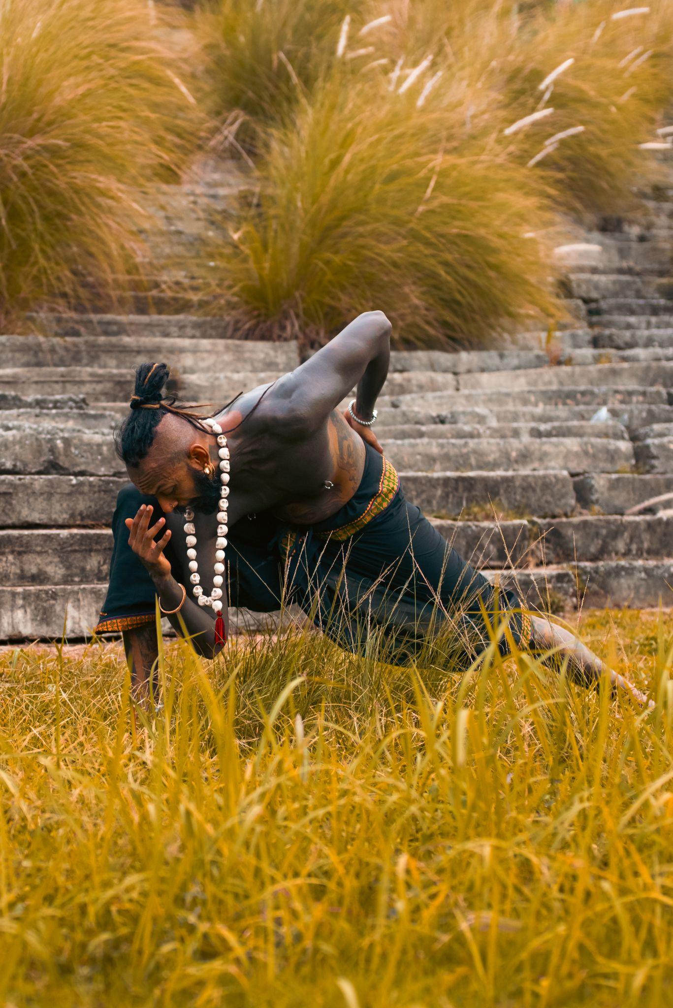 A performer in traditional attire striking a dynamic pose among tall grass