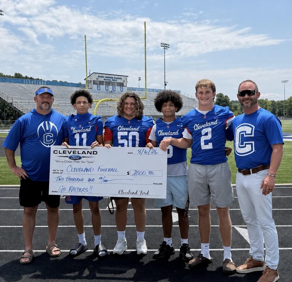 Group of football players and coaches holding a large check on a field