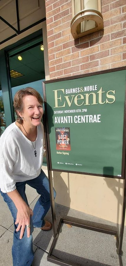 A woman smiles next to an events sign for a book signing at Barnes & Noble