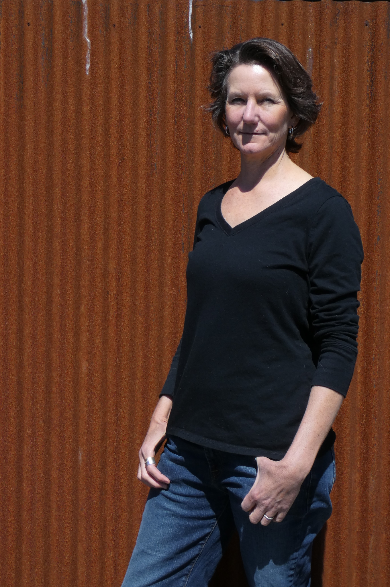 A woman in a black shirt stands confidently against a rust-colored corrugated background