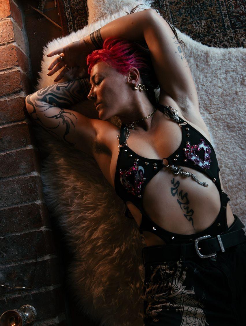 Person with pink hair and tattoos lying on a furry surface against a brick wall