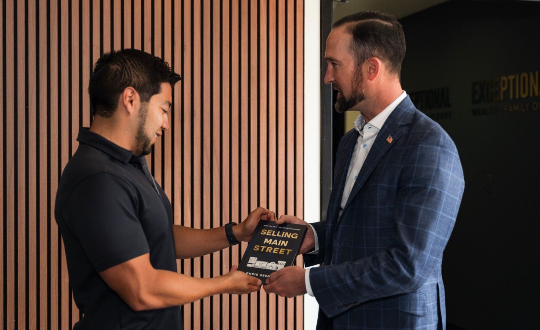 Two men exchanging a book titled "Selling Main Street" in an office setting
