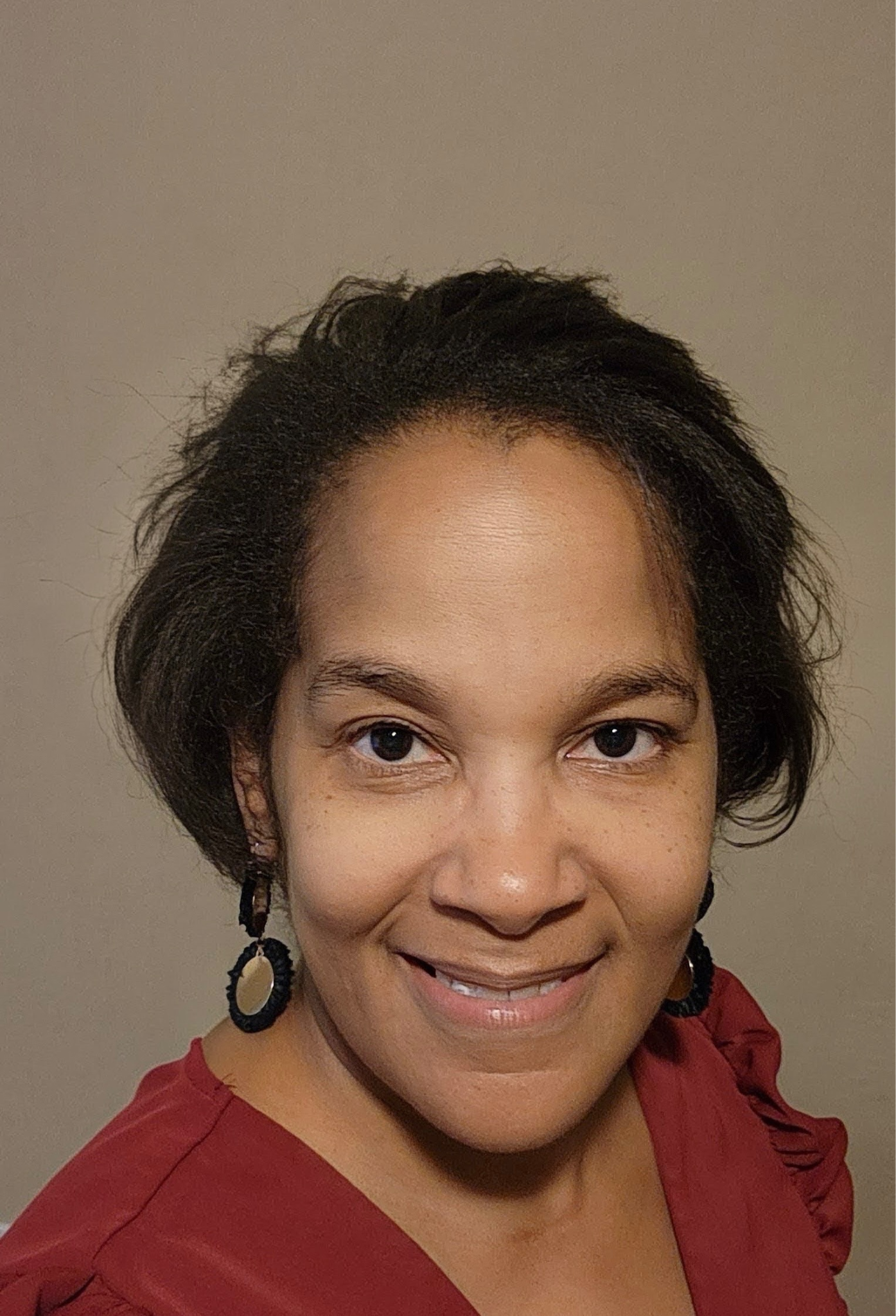 A woman with short hair smiling, wearing a red top and hoop earrings