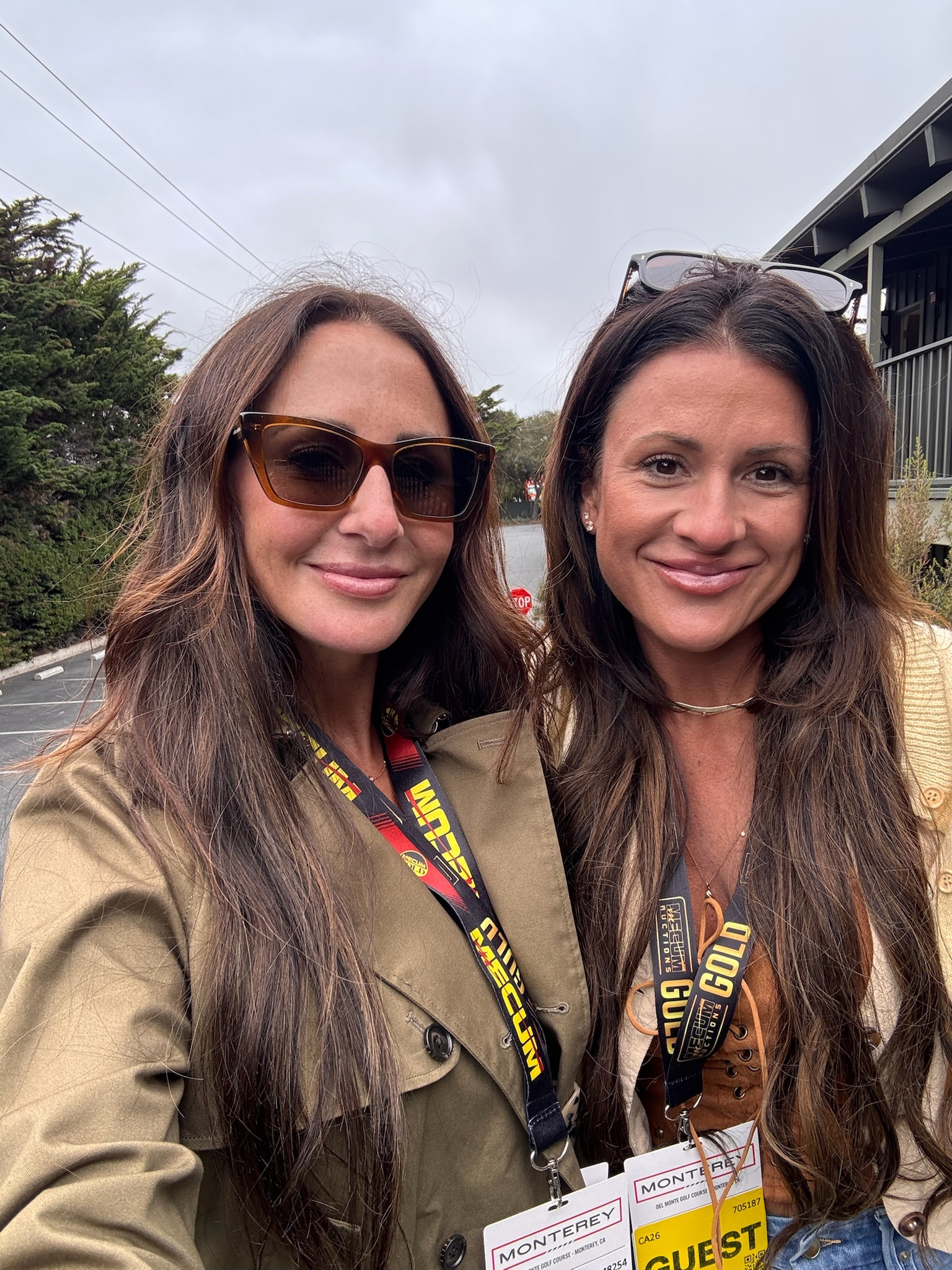Two women posing for a selfie, wearing sunglasses and event lanyards outdoors