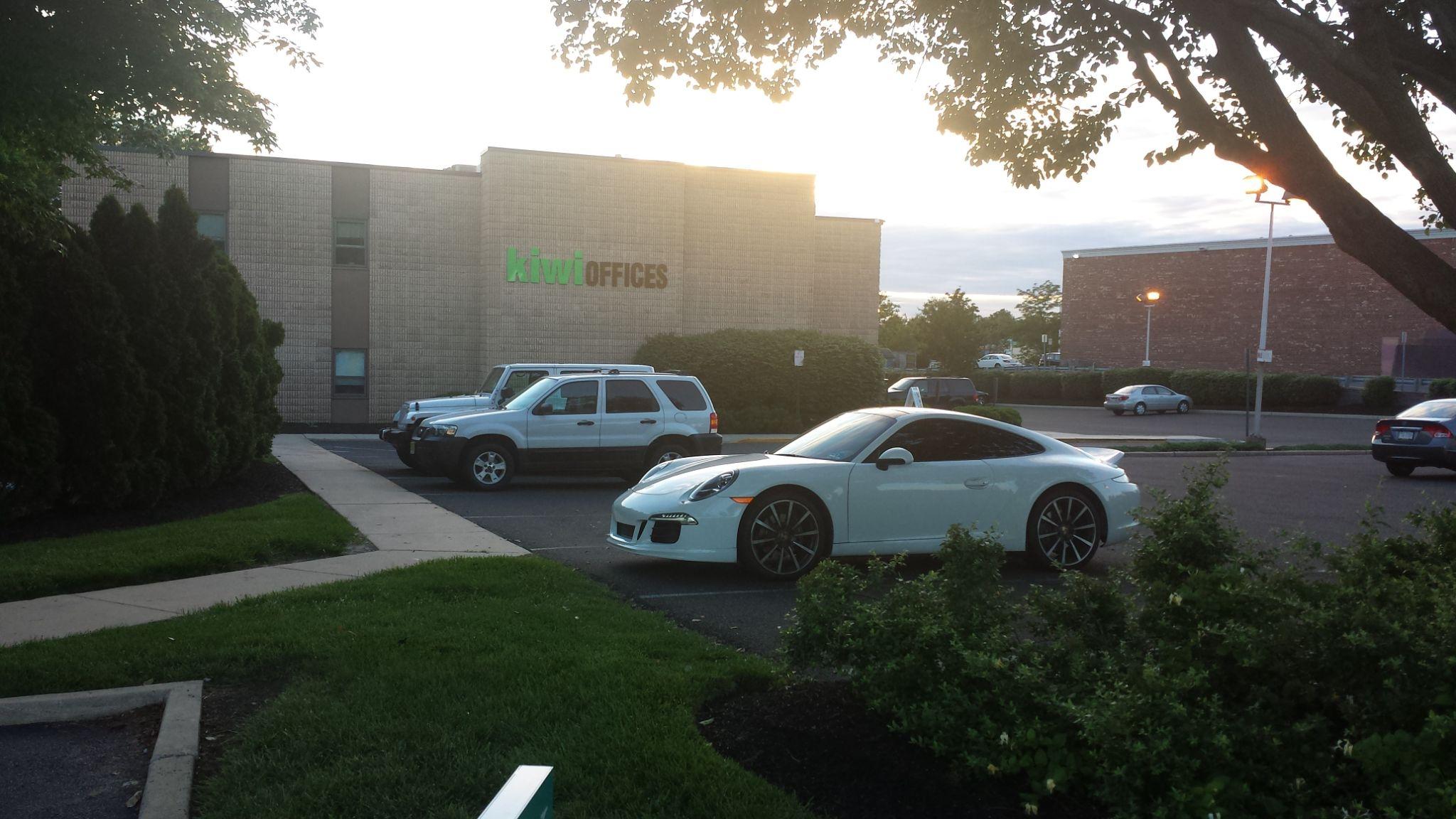 A white sports car parked in front of an office building with green signage