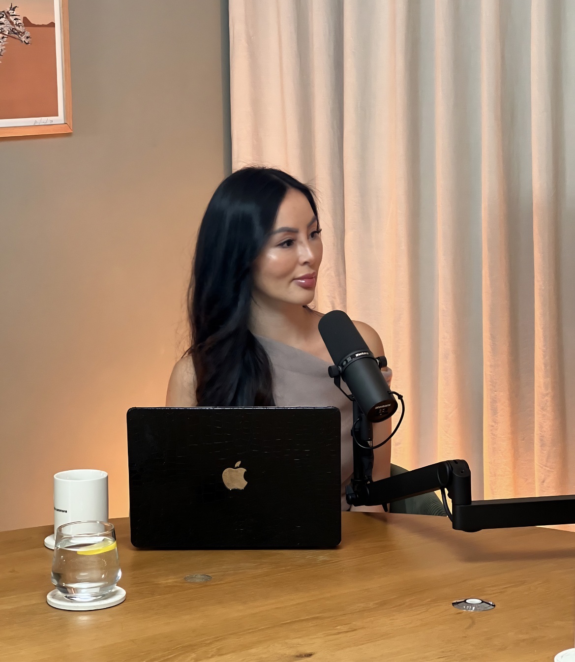 A woman sitting at a table with a laptop, microphone, and glass of water