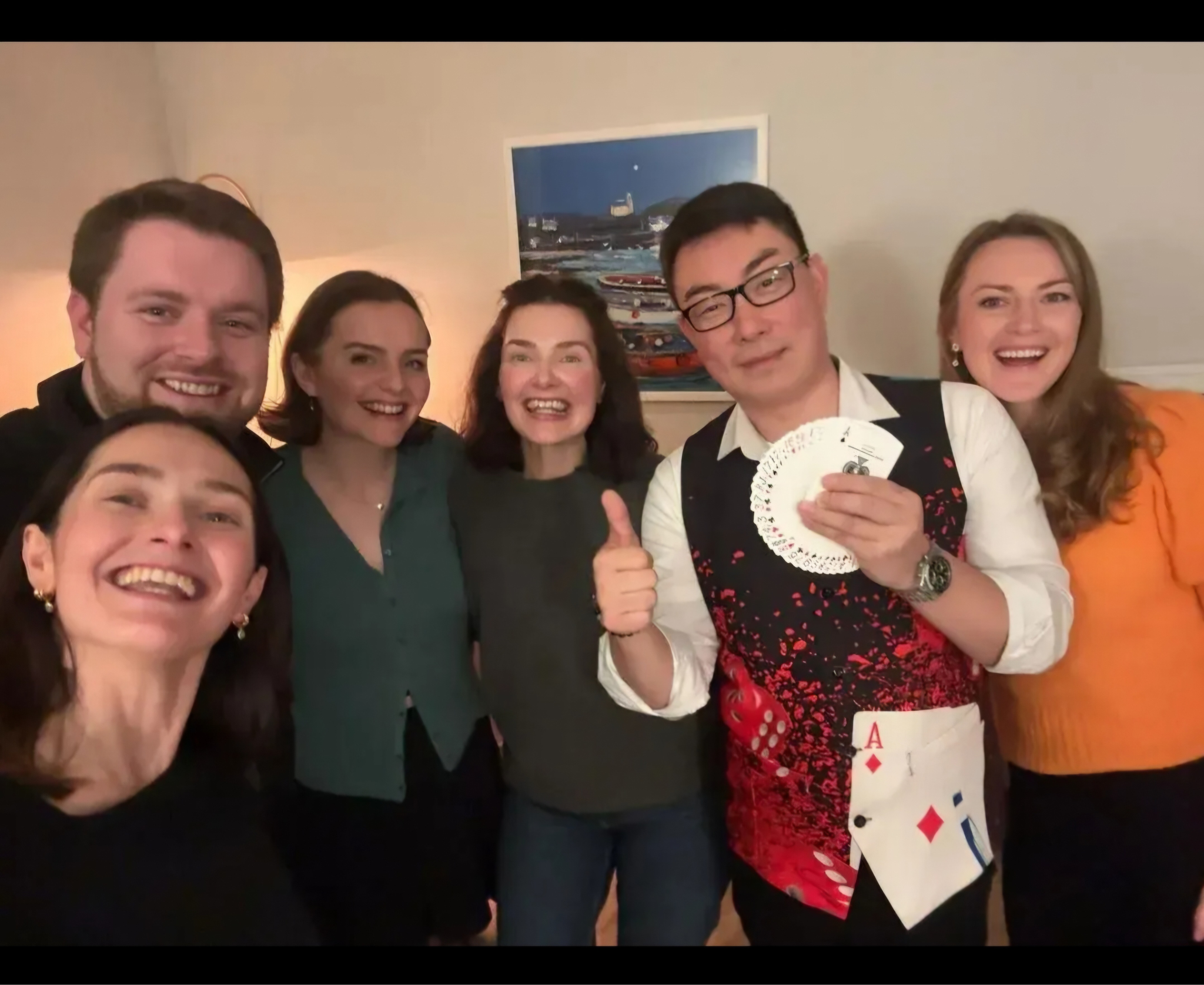 A group of six people posing together, smiling, with one holding playing cards