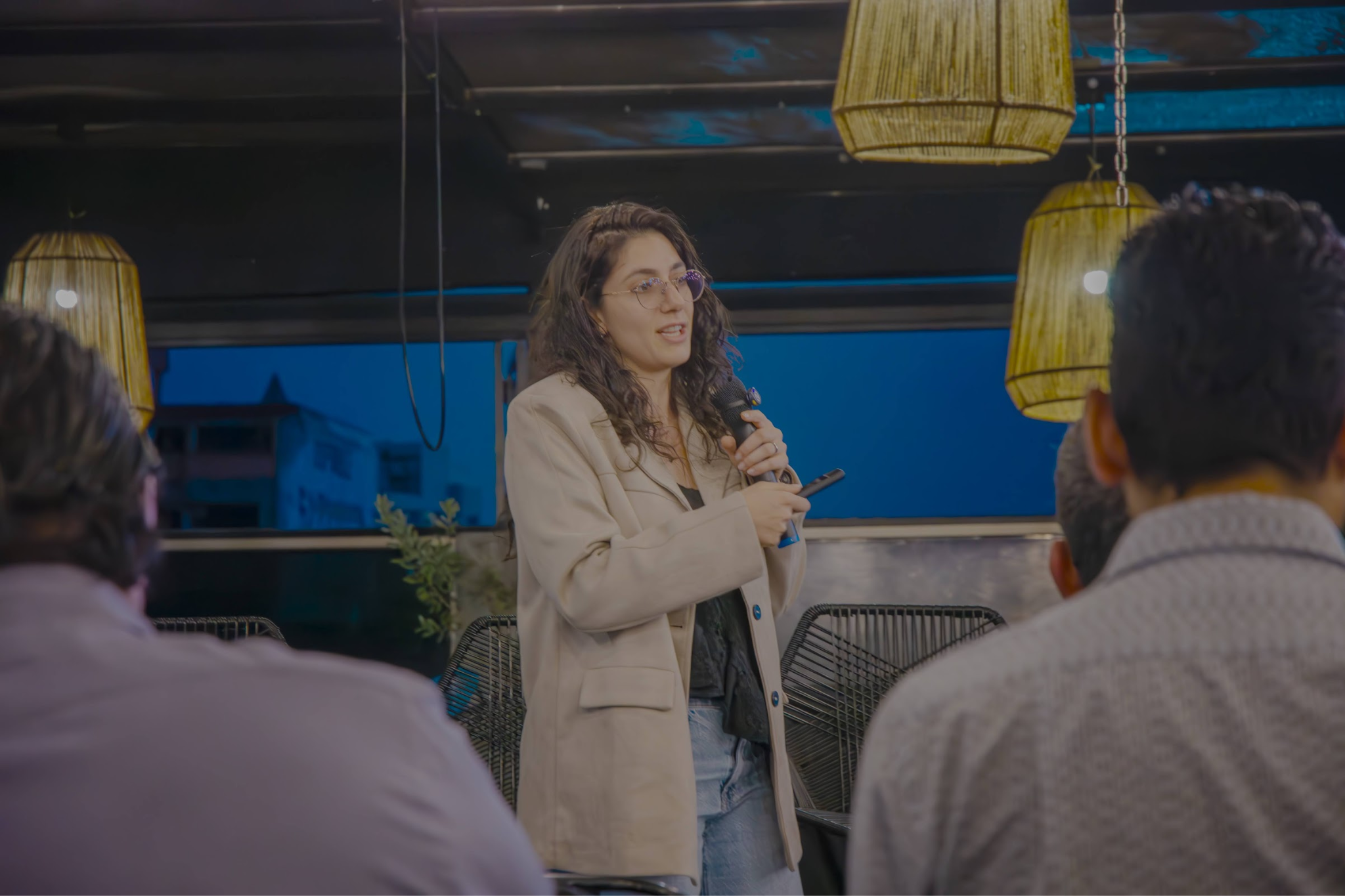 A woman with curly hair speaks to an audience in a modern setting