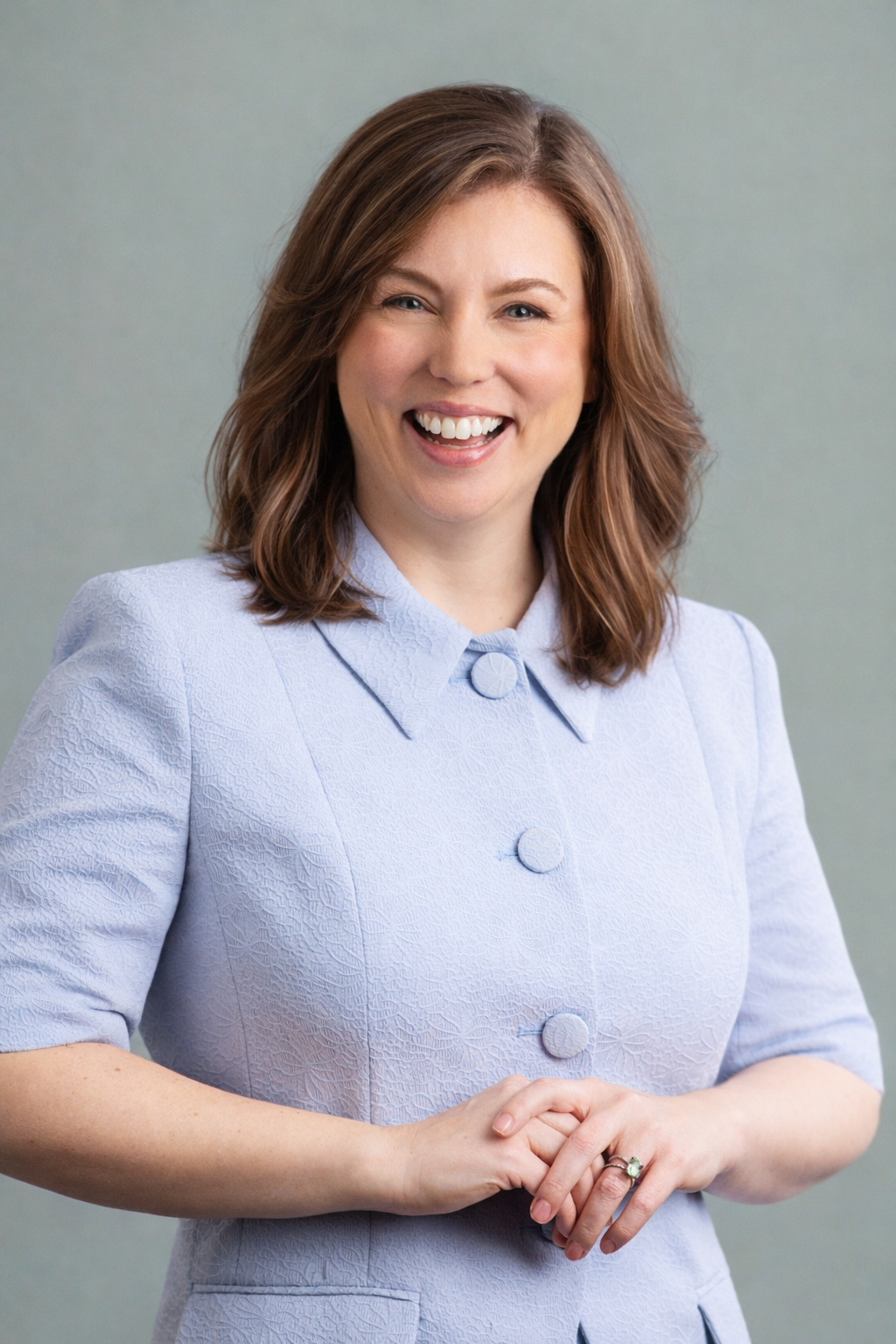 Smiling woman in a light blue blazer with short sleeves, hands clasped together