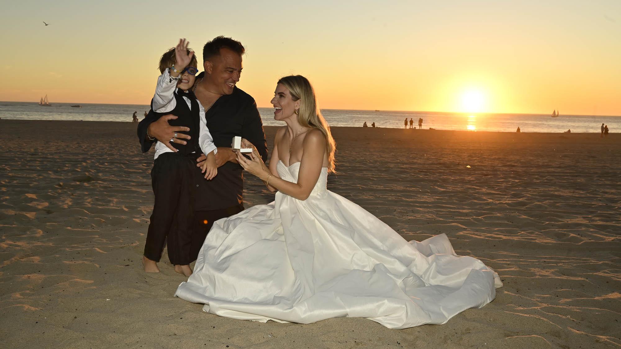 A couple with a child on the beach at sunset, celebrating their engagement.