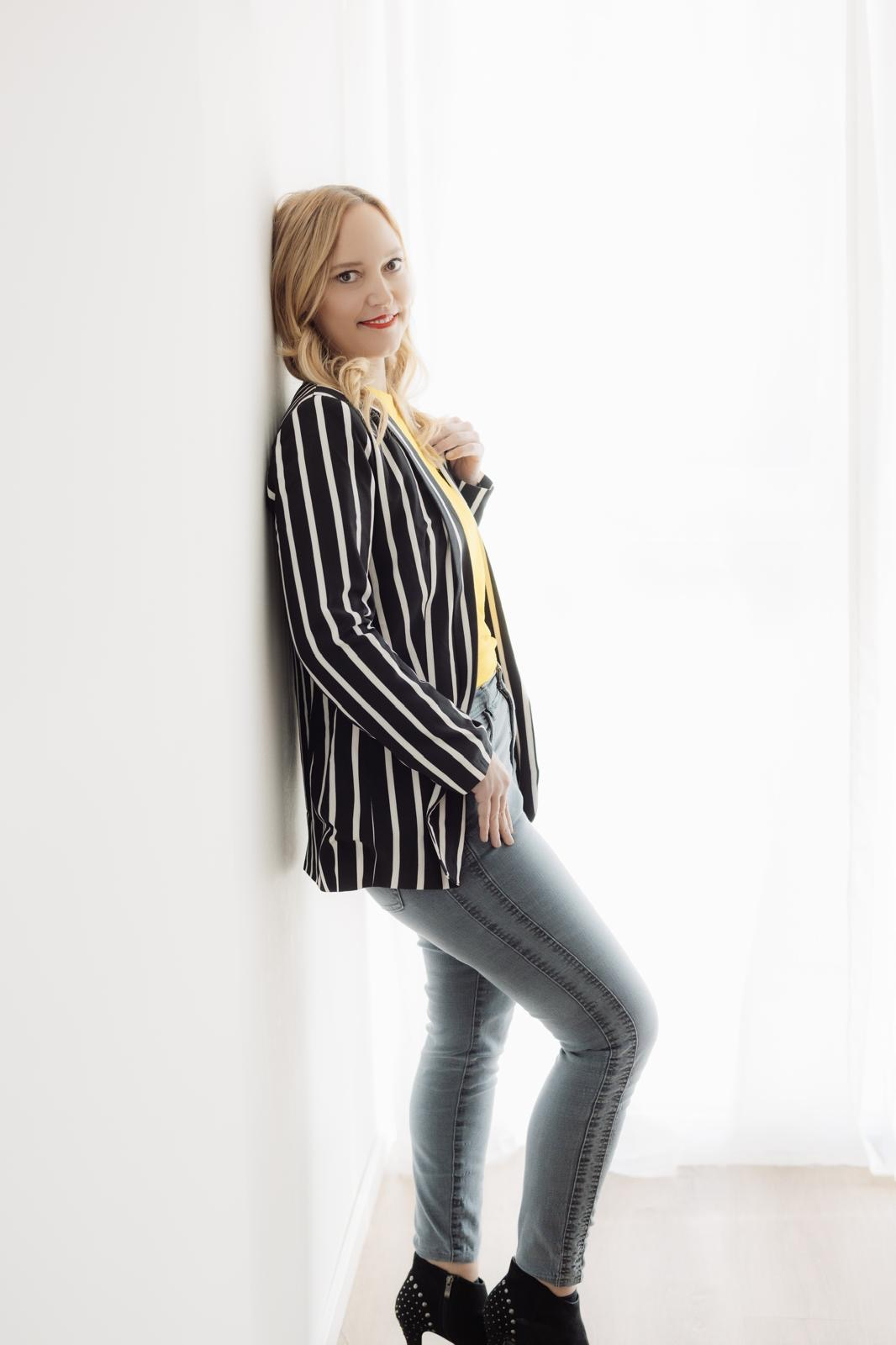 Woman in striped blazer and yellow top poses against a bright background