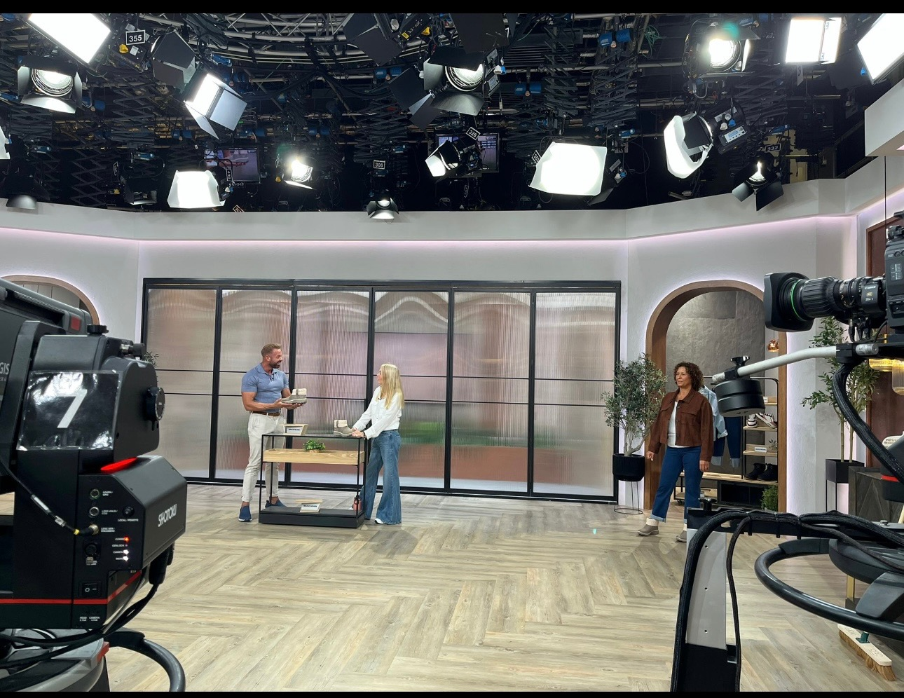 Television studio set with three presenters and various cameras arranged around.