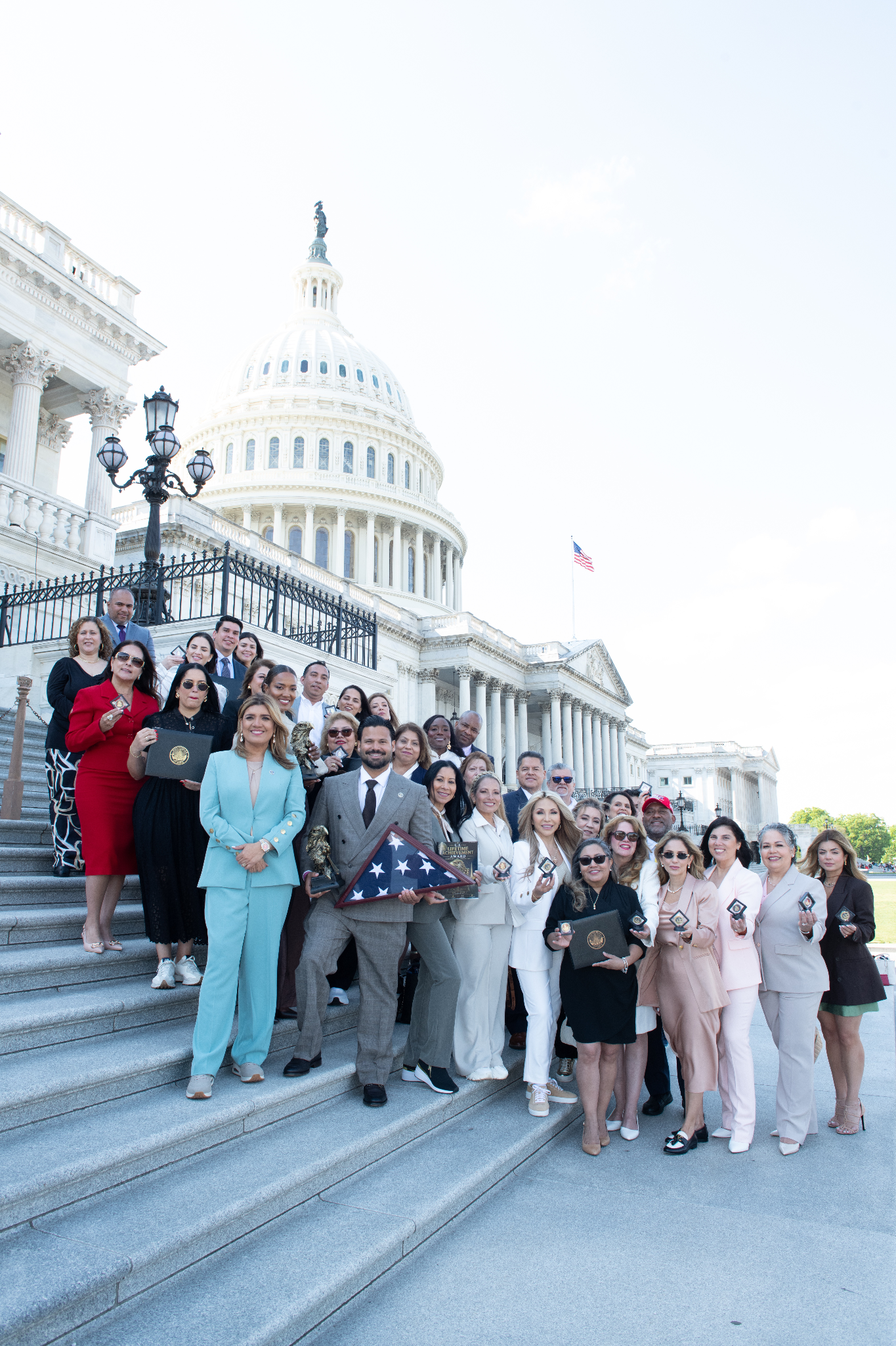 Group of diverse individuals posing at the U.S. Capitol steps with awards and flags