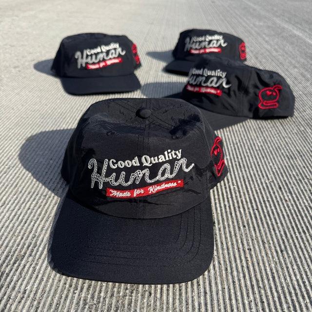 Several black caps featuring "Good Quality Human" and playful logos on the side