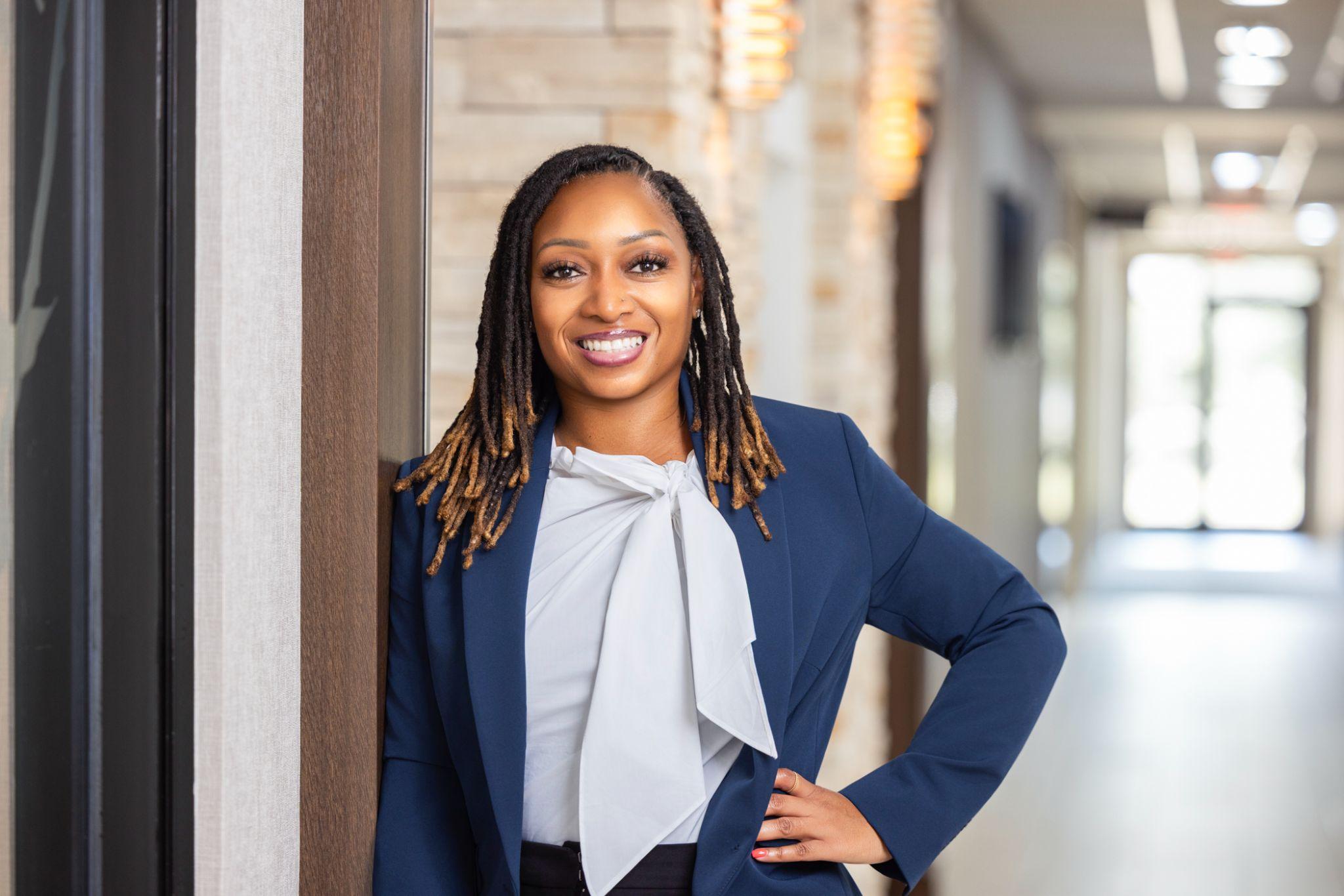 Smiling professional woman in a navy blazer stands in a bright corridor.