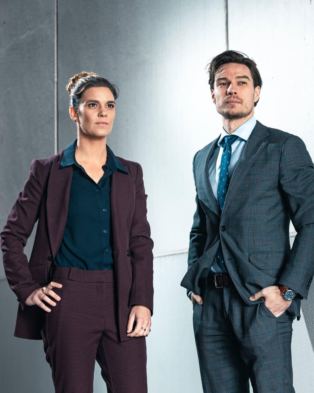 Two business professionals in tailored suits posing confidently against a modern background