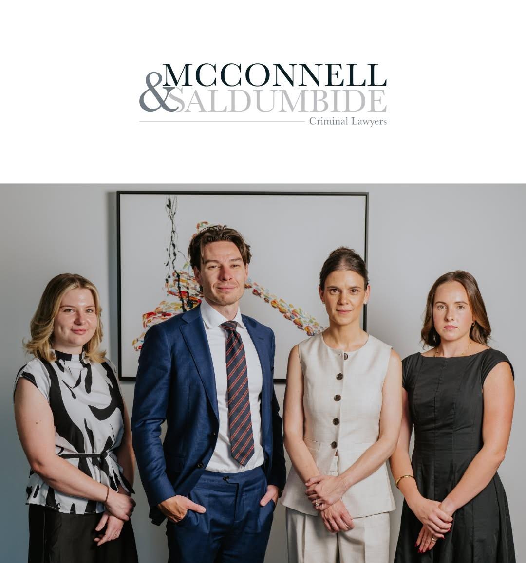Four professionals standing together in an office setting, smiling at the camera