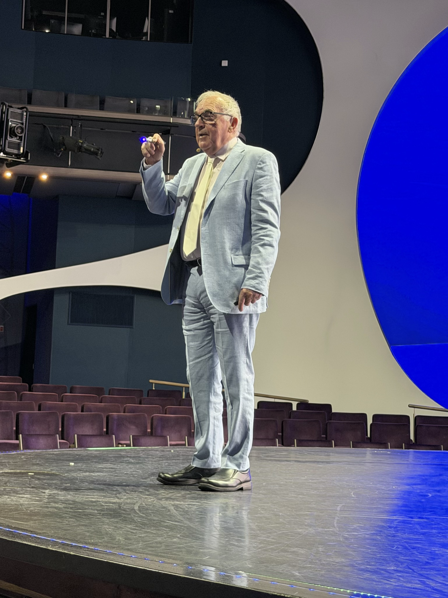 Man in a light blue suit stands on stage giving a presentation.