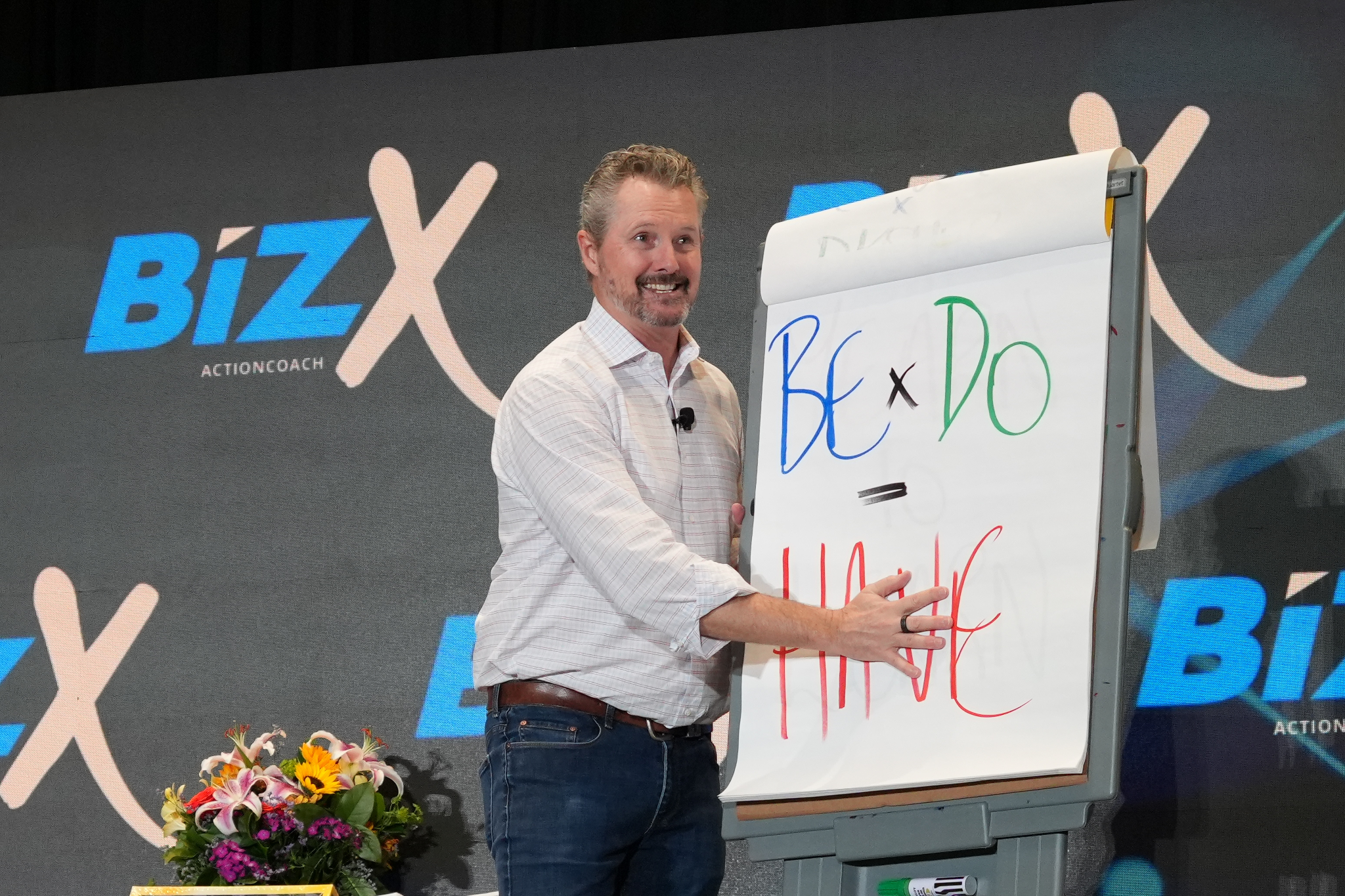 A speaker presenting on a whiteboard with colorful text at a BizX event