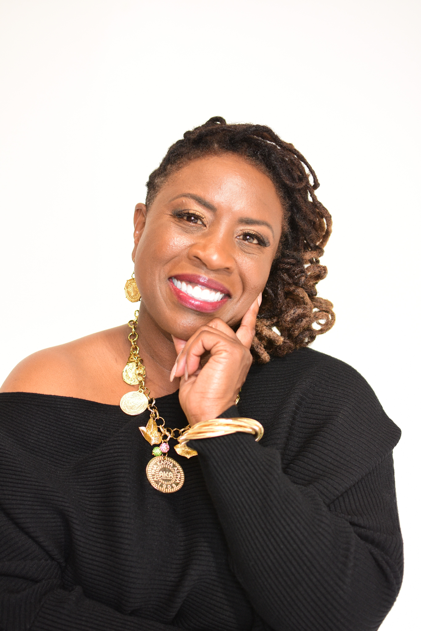 Smiling woman with dreadlocks wearing a black sweater and statement jewelry