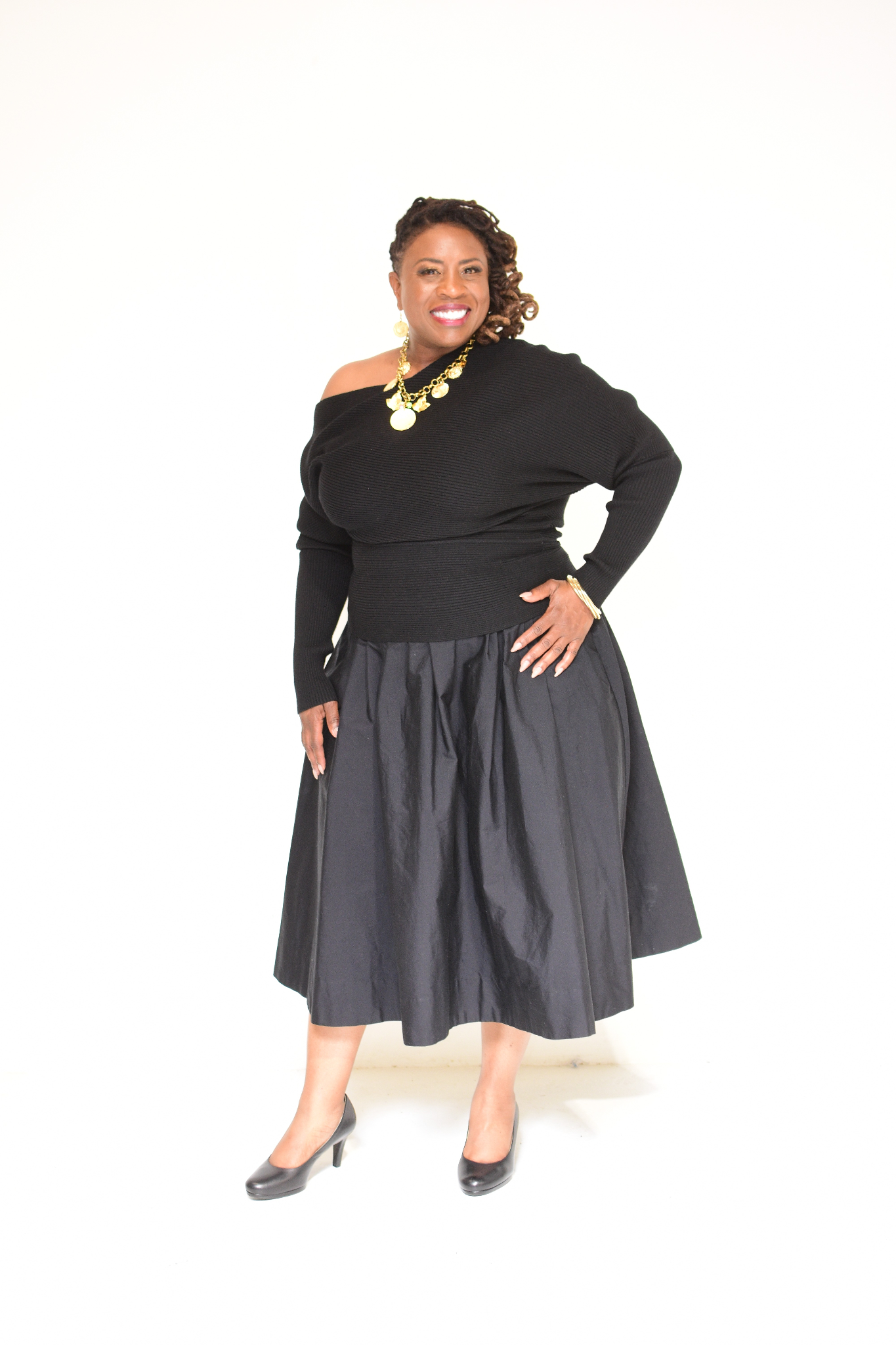 Smiling woman in black off-shoulder top and full black skirt posing confidently