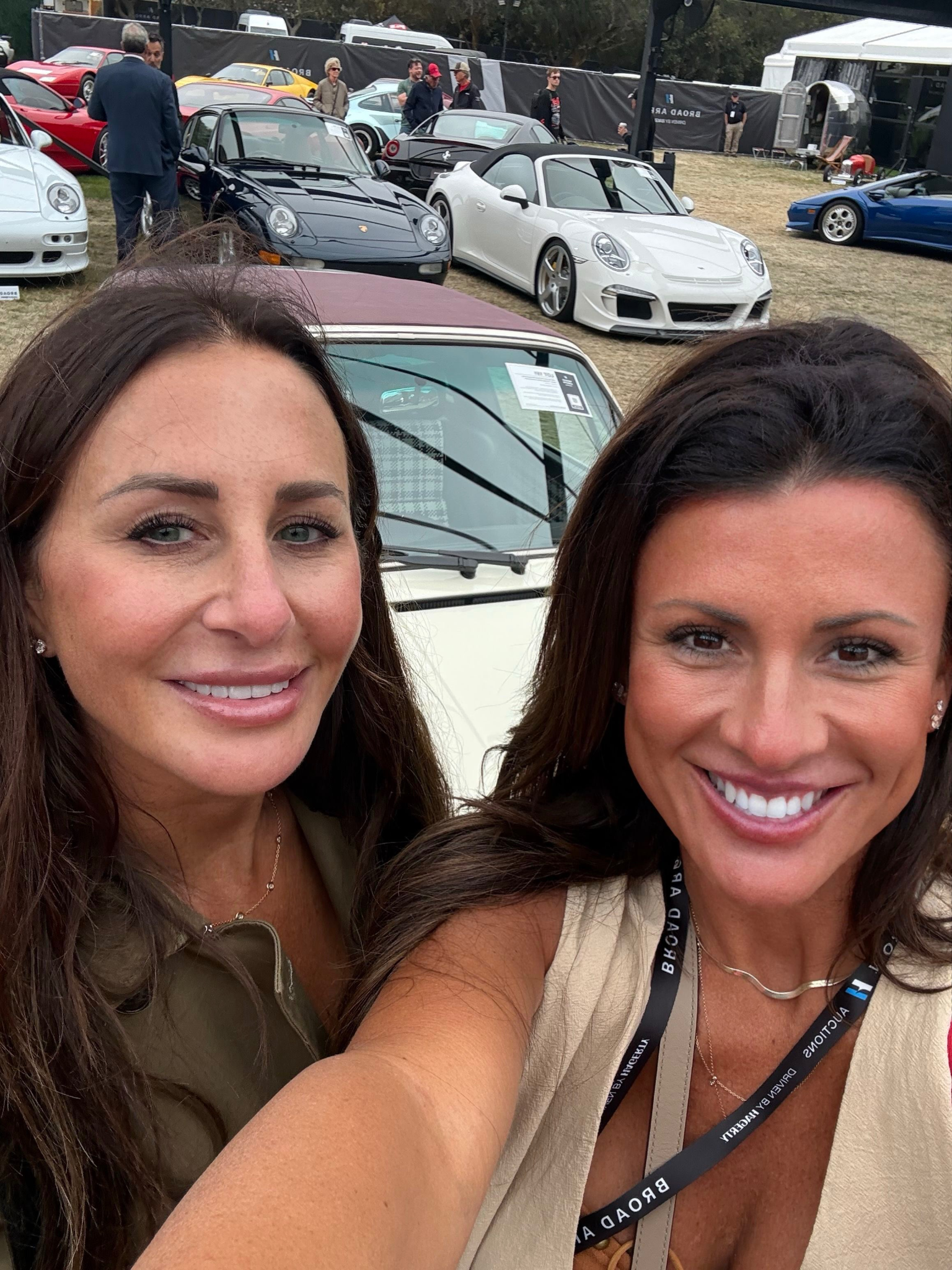 Two women smiling in front of a variety of cars at an event