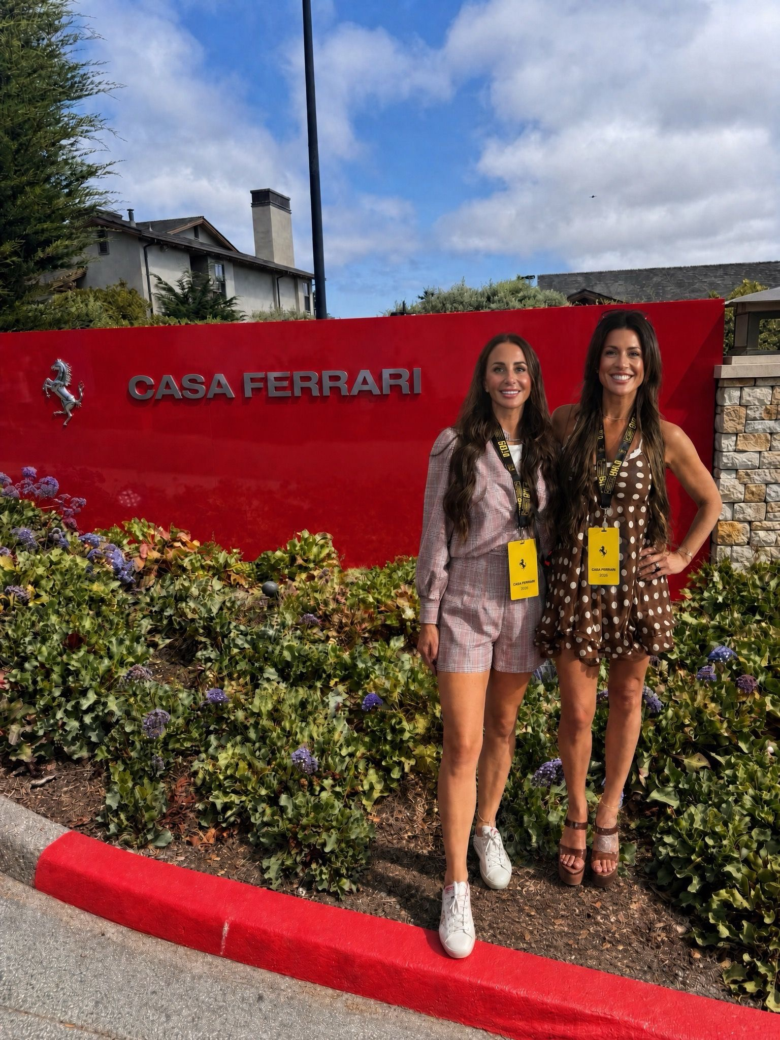 Two women pose in front of the Casa Ferrari sign with colorful flowers nearby