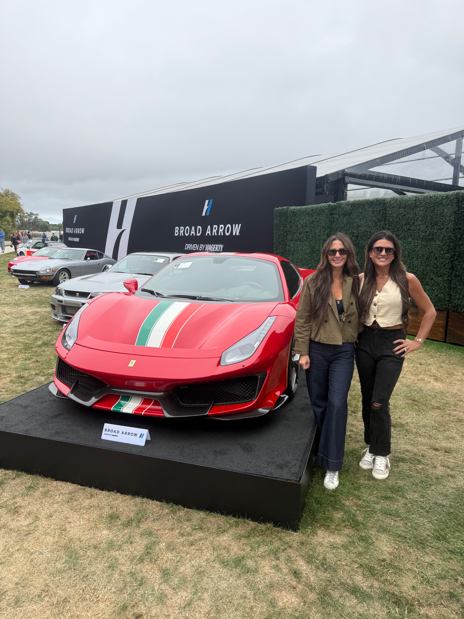 Two women pose next to a red Ferrari 488 Pista at an outdoor event