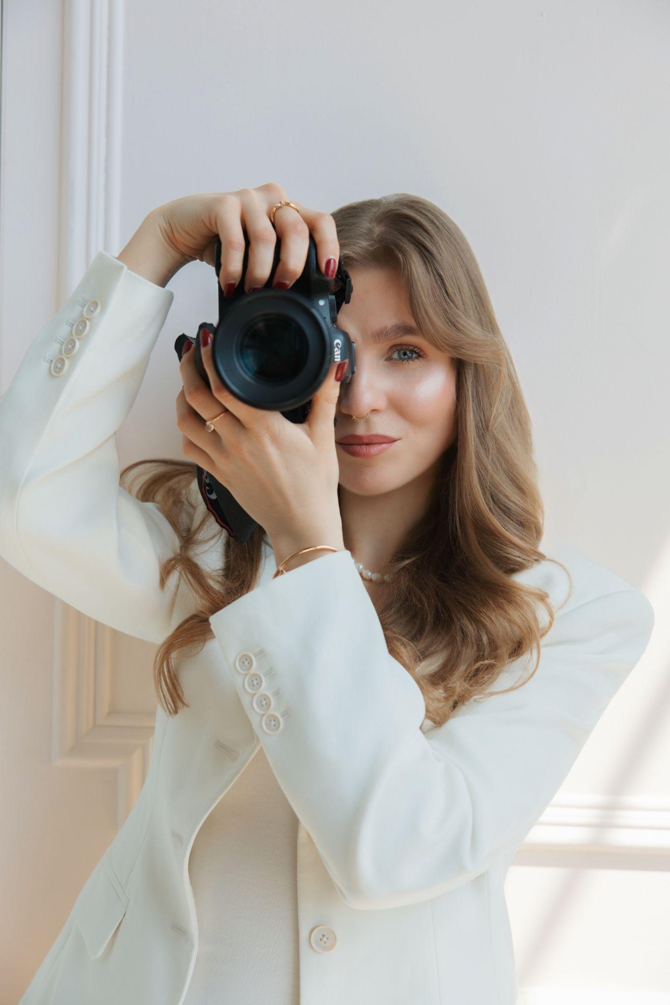 Woman in a white blazer holding a camera and posing confidently
