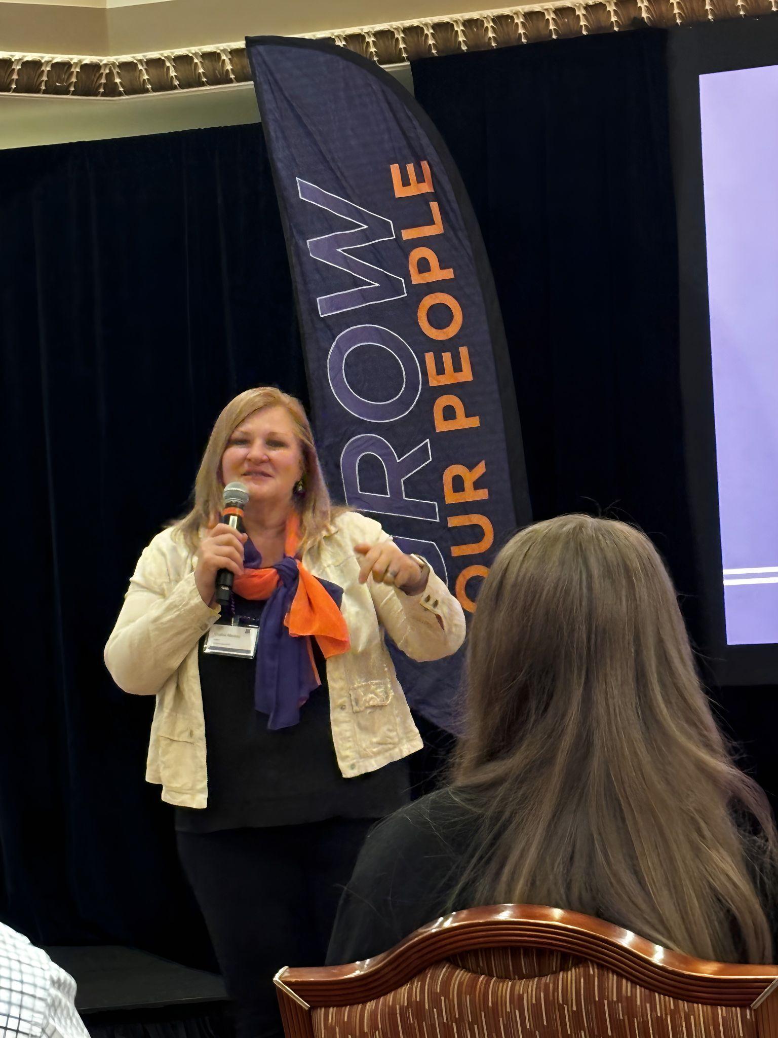 A speaker on stage holding a microphone, engaging with an audience in a conference setting